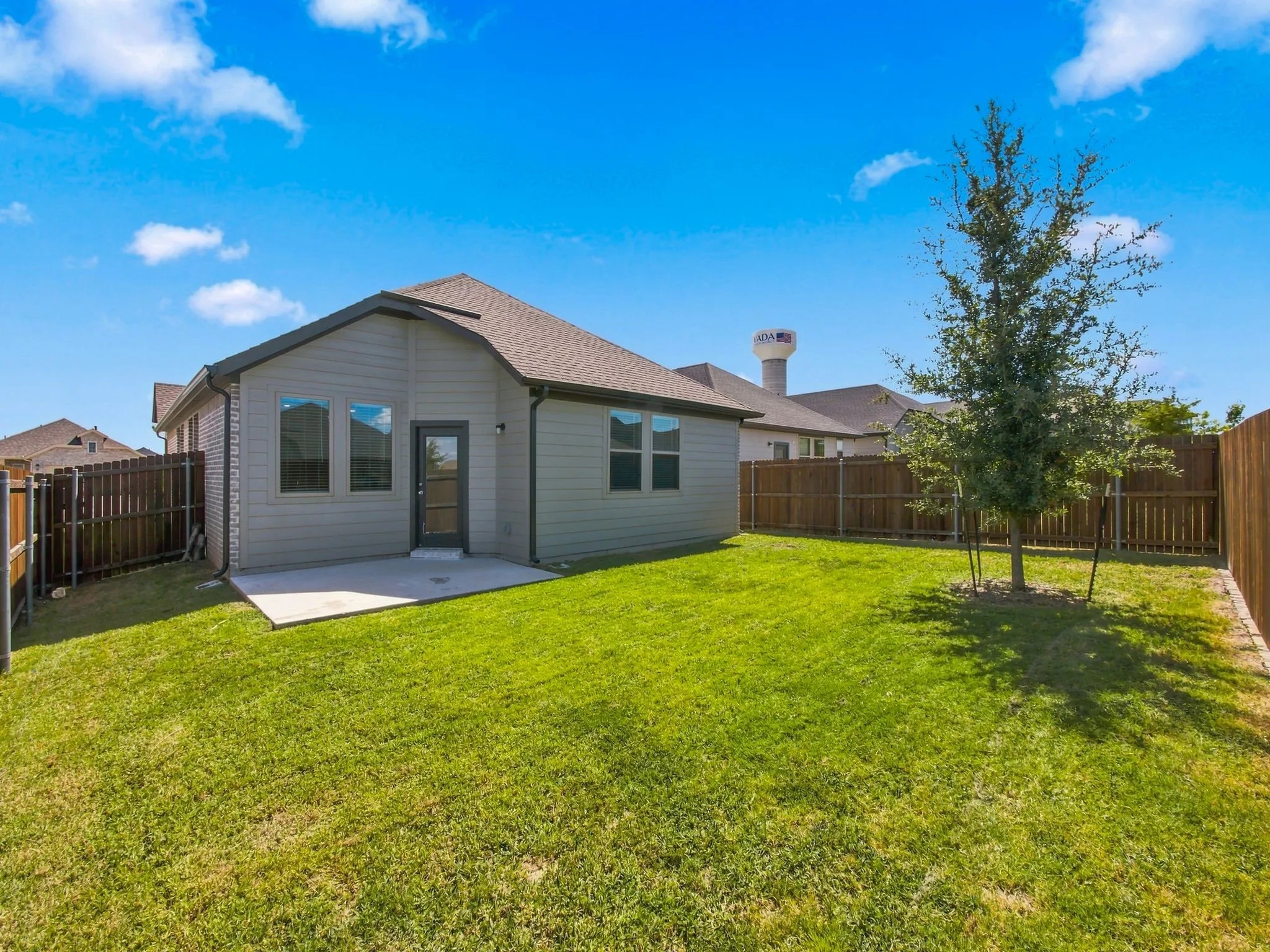 Expansive backyard featuring a concrete patio, a young tree, and wood fencing