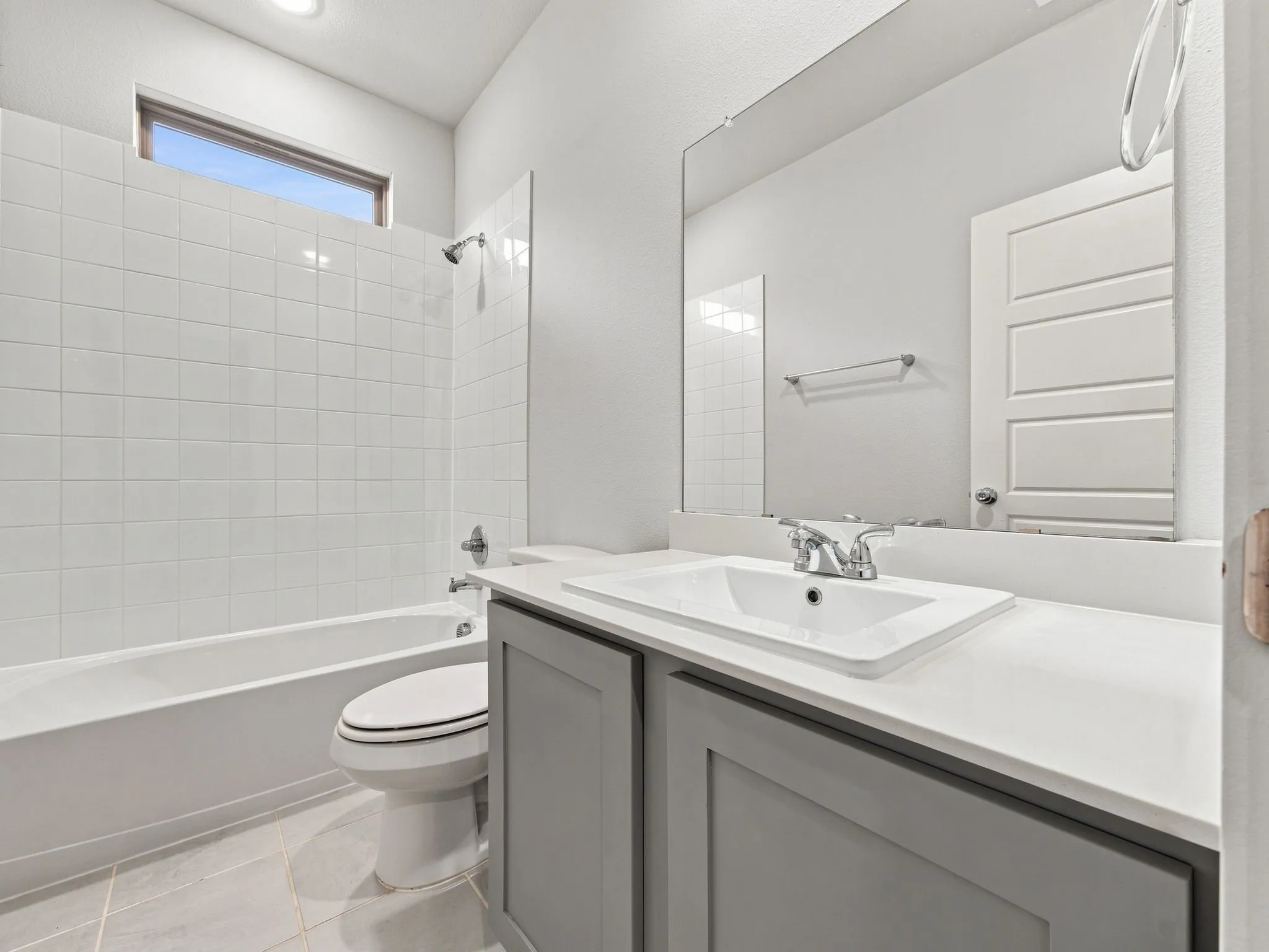 Bathroom featuring a built-in bathtub with shower, white square wall tile, a gray vanity with a single basin sink, an expansive mirror, and tile flooring