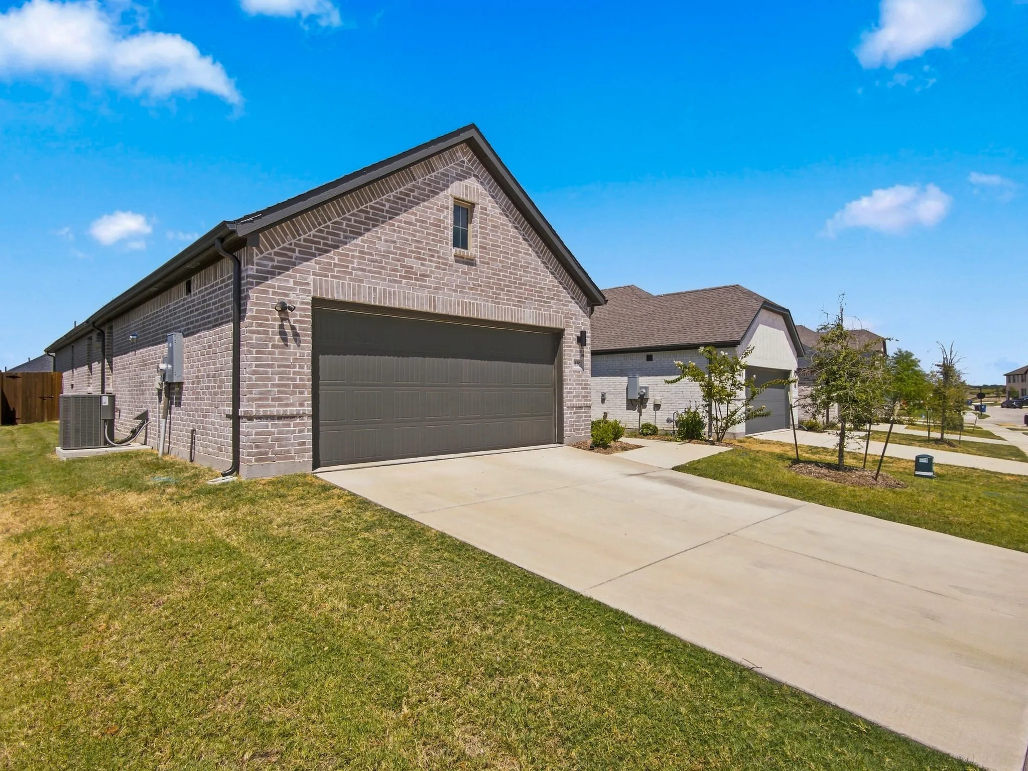 Brick exterior with a gabled roofline, featuring a two-car garage with a dark panel door, and a concrete driveway