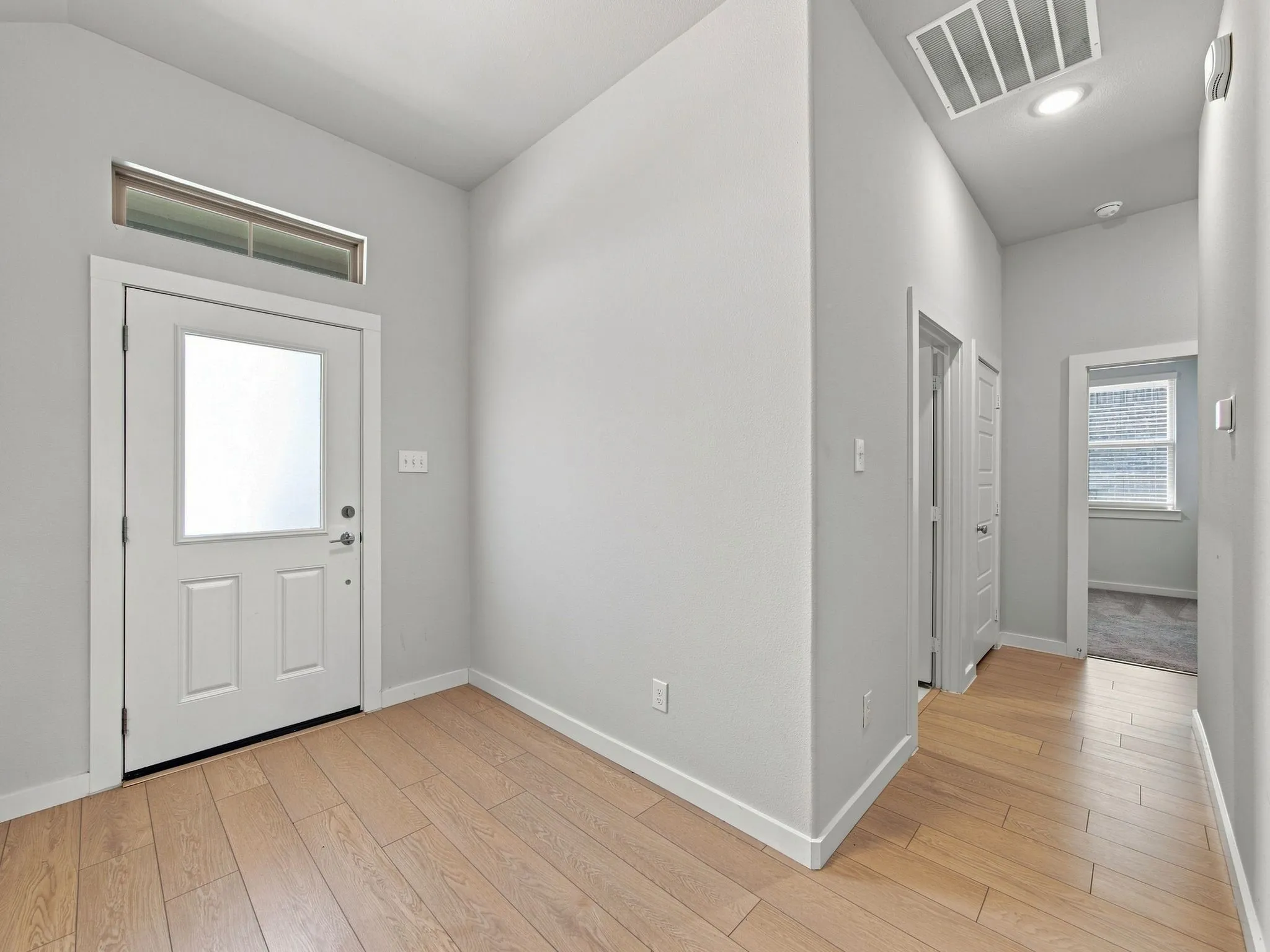 Wood-finish flooring, white paneled door with frosted glass insert, transom window, recessed ceiling lighting, and white trim