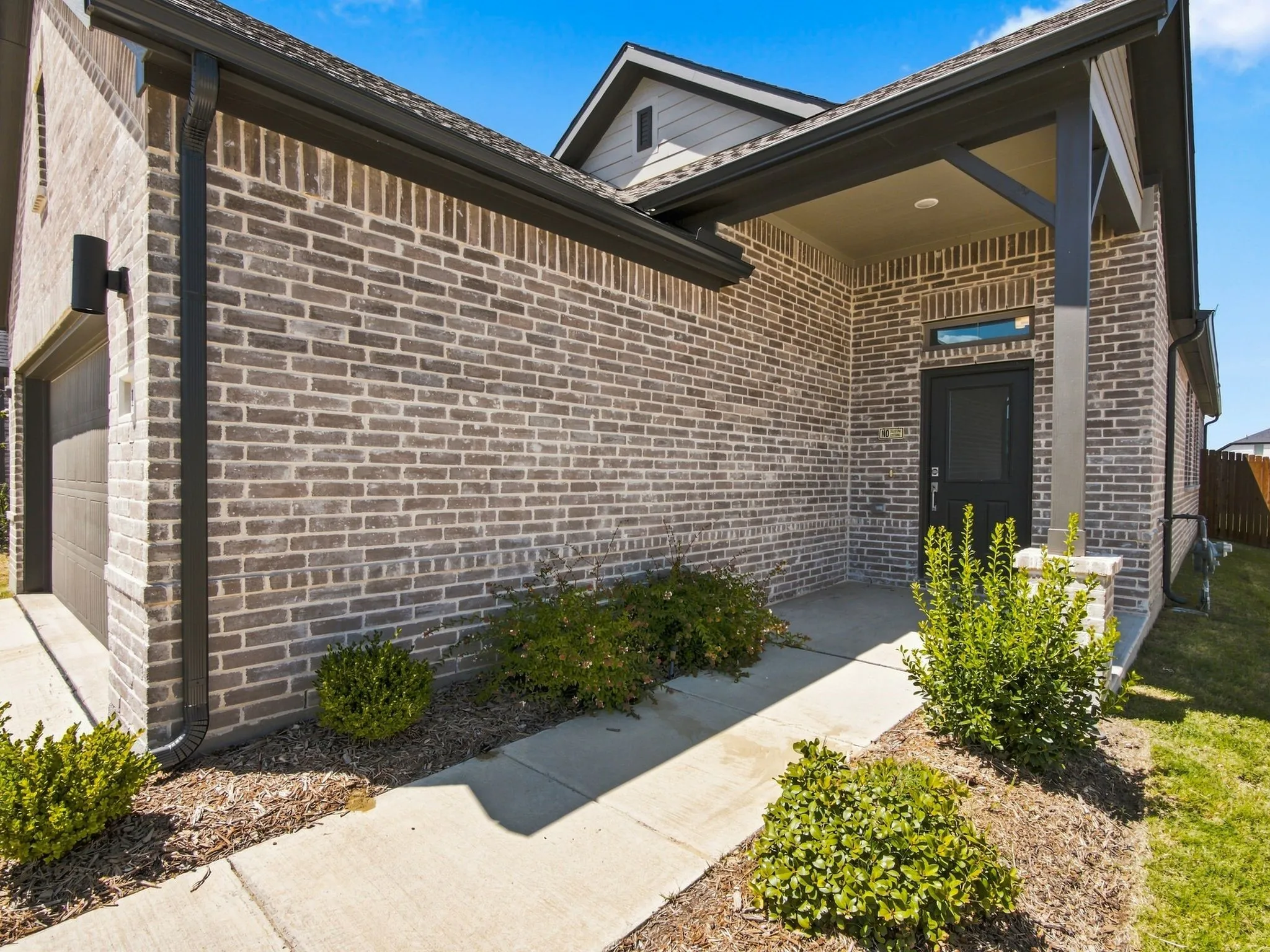Brick exterior with contrasting dark trim, covered entry porch, dark-paneled front door, and mature landscaping
