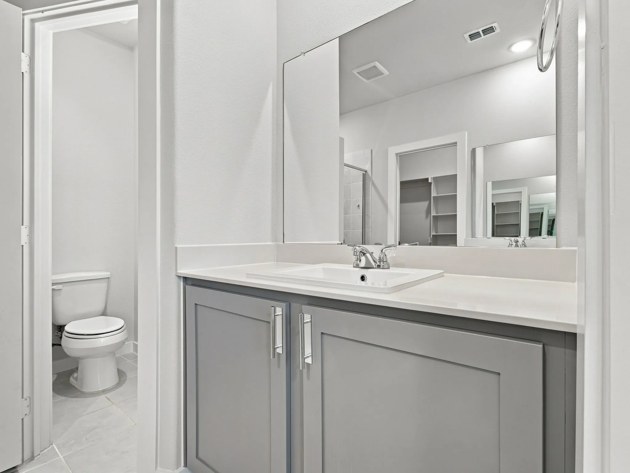 White rectangular sink with chrome faucet, light grey shaker-style vanity with chrome hardware, and a large frameless mirror