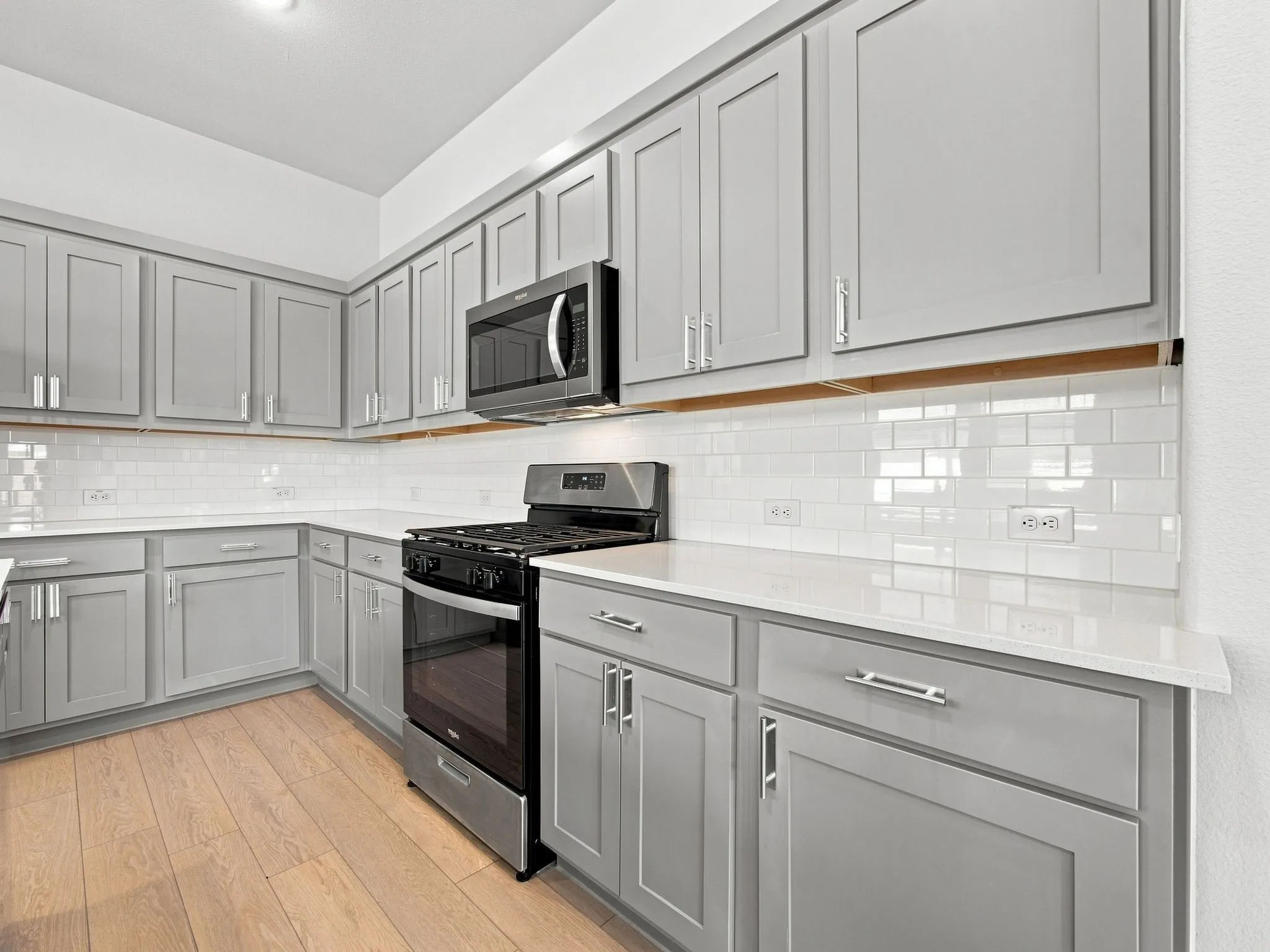Kitchen featuring extensive gray shaker cabinetry, white subway tile backsplash, white countertops, stainless steel appliances, and wood-finish flooring