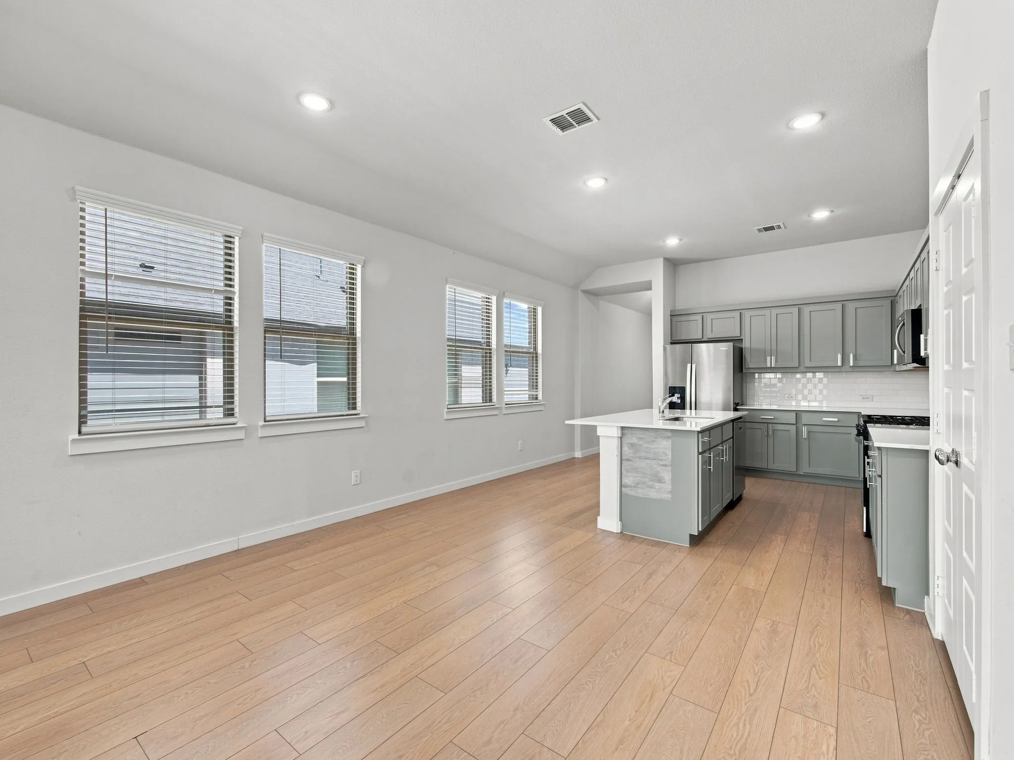 Recessed lighting, wood-finish flooring, kitchen island with seating, stainless steel appliances, and a tiled backsplash