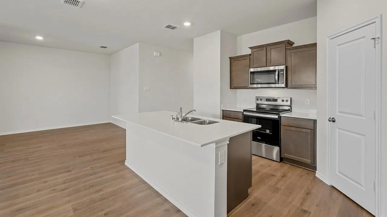 Kitchen island with an undermount sink, stainless steel appliances, wood-finish flooring, recessed lighting, and white walls
