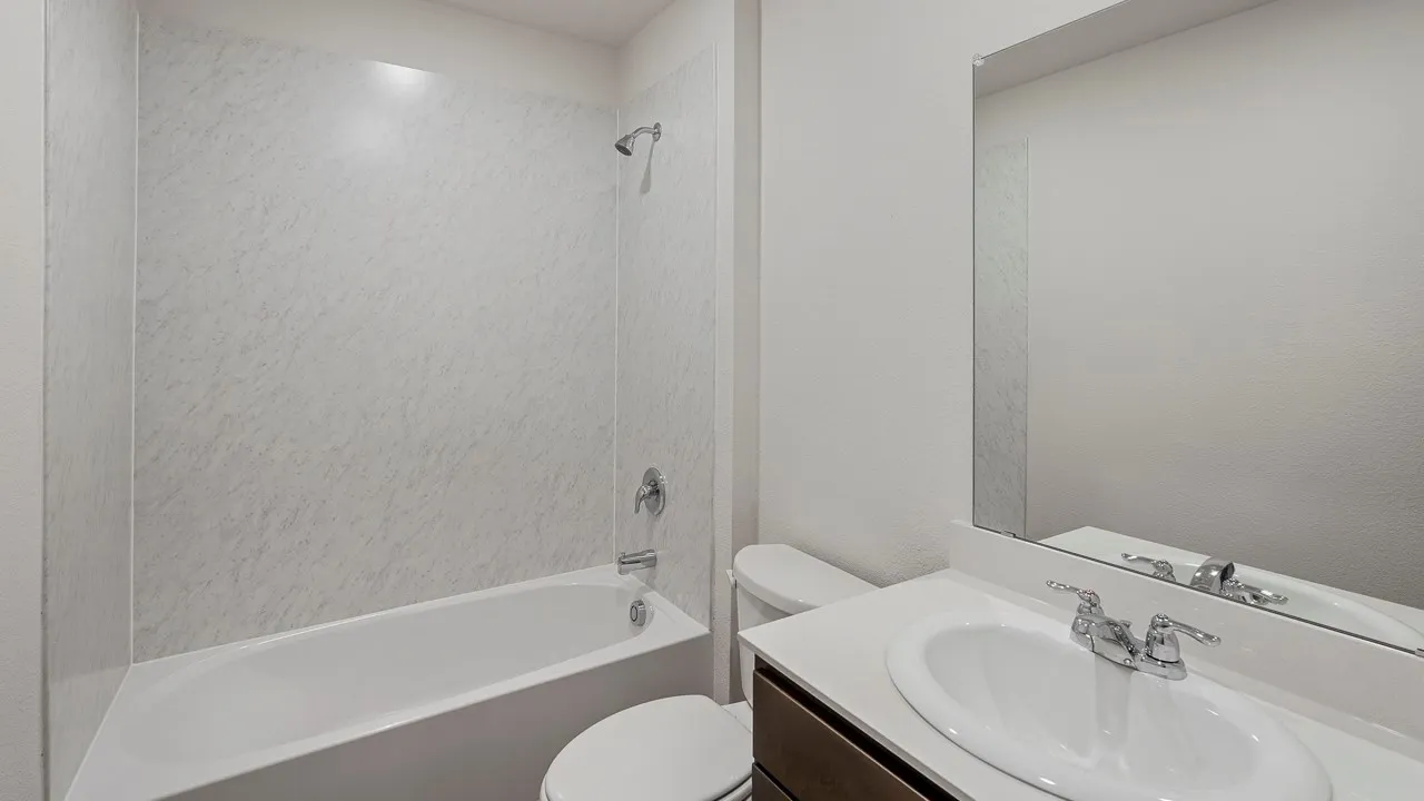 White bathtub with integrated shower, chrome fixtures, a modern vanity with an integrated sink, and a large wall-mounted mirror