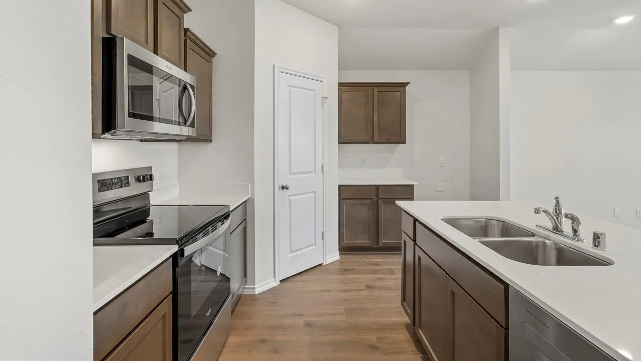 Stainless steel appliances, wood-finish flooring, white countertops, dark wood cabinetry, and a double basin sink