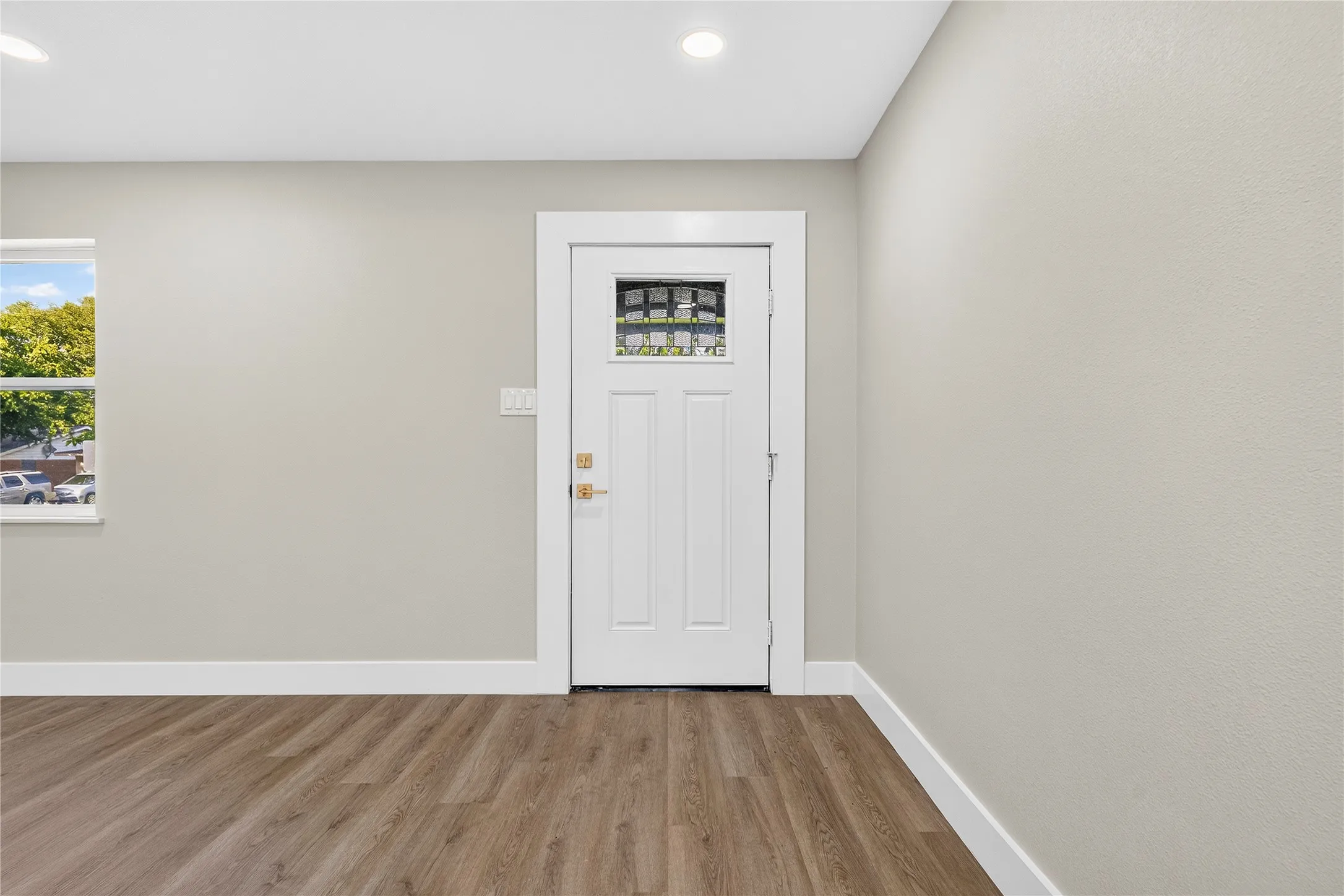 Wood-finish flooring, recessed lighting, neutral wall tones, white trim, and a paneled door with decorative glass inserts