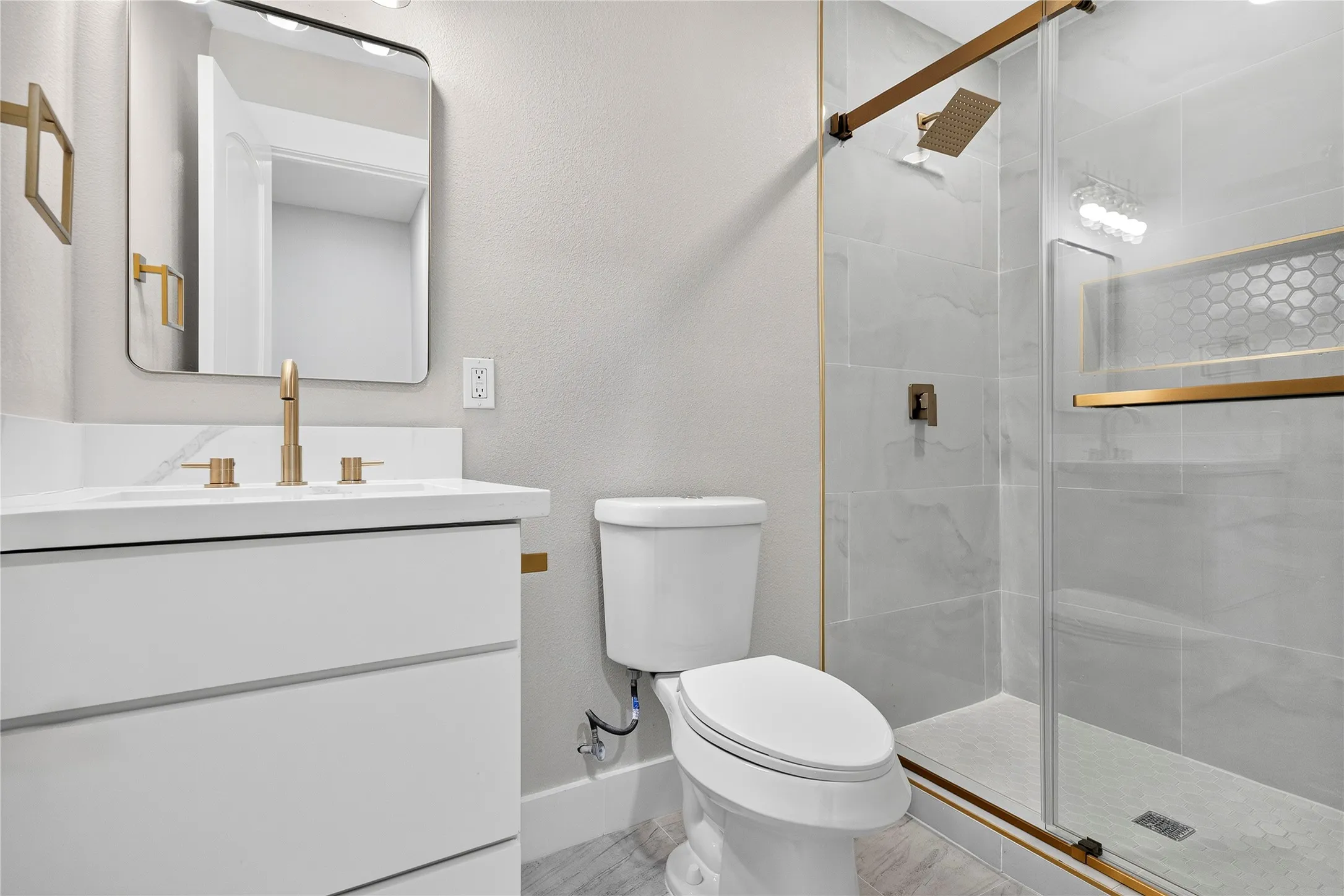Frameless glass shower enclosure with brass hardware, a built-in hexagonal tile niche, and a rain showerhead