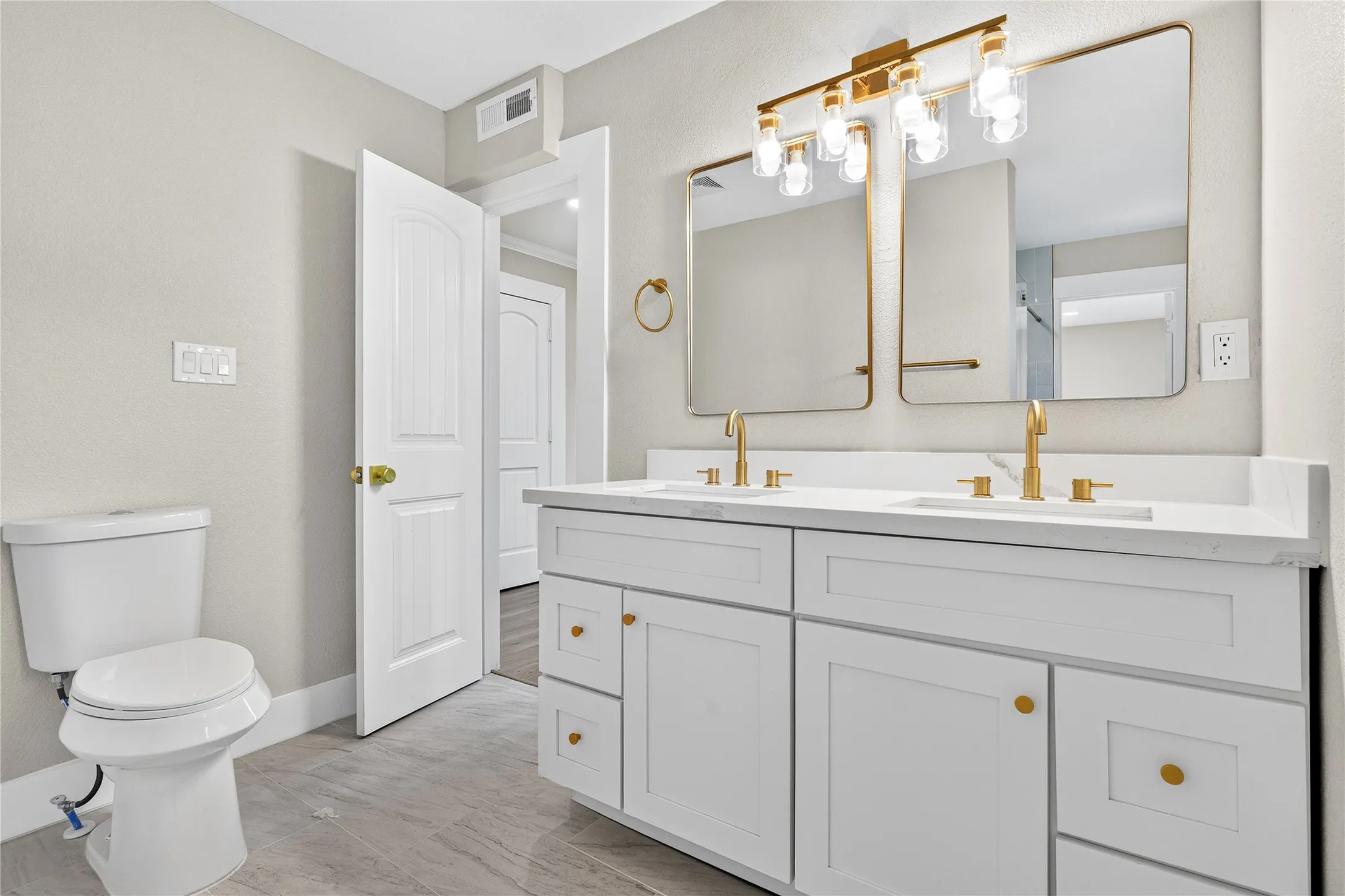 Dual white vanities with gold-finish hardware, individual framed mirrors, gold-finish light fixture, and white countertop