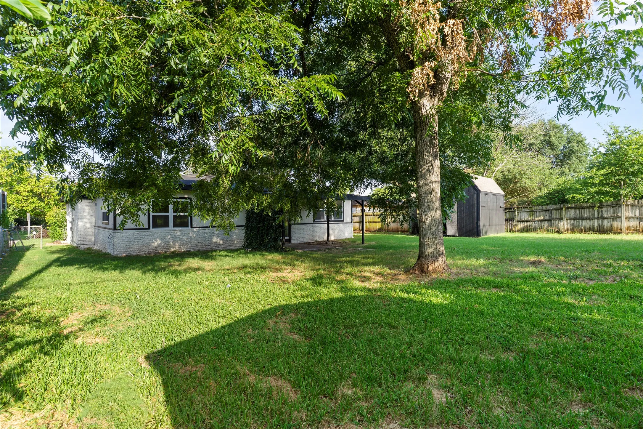 Expansive backyard with mature trees, a storage shed, and a wooden perimeter fence