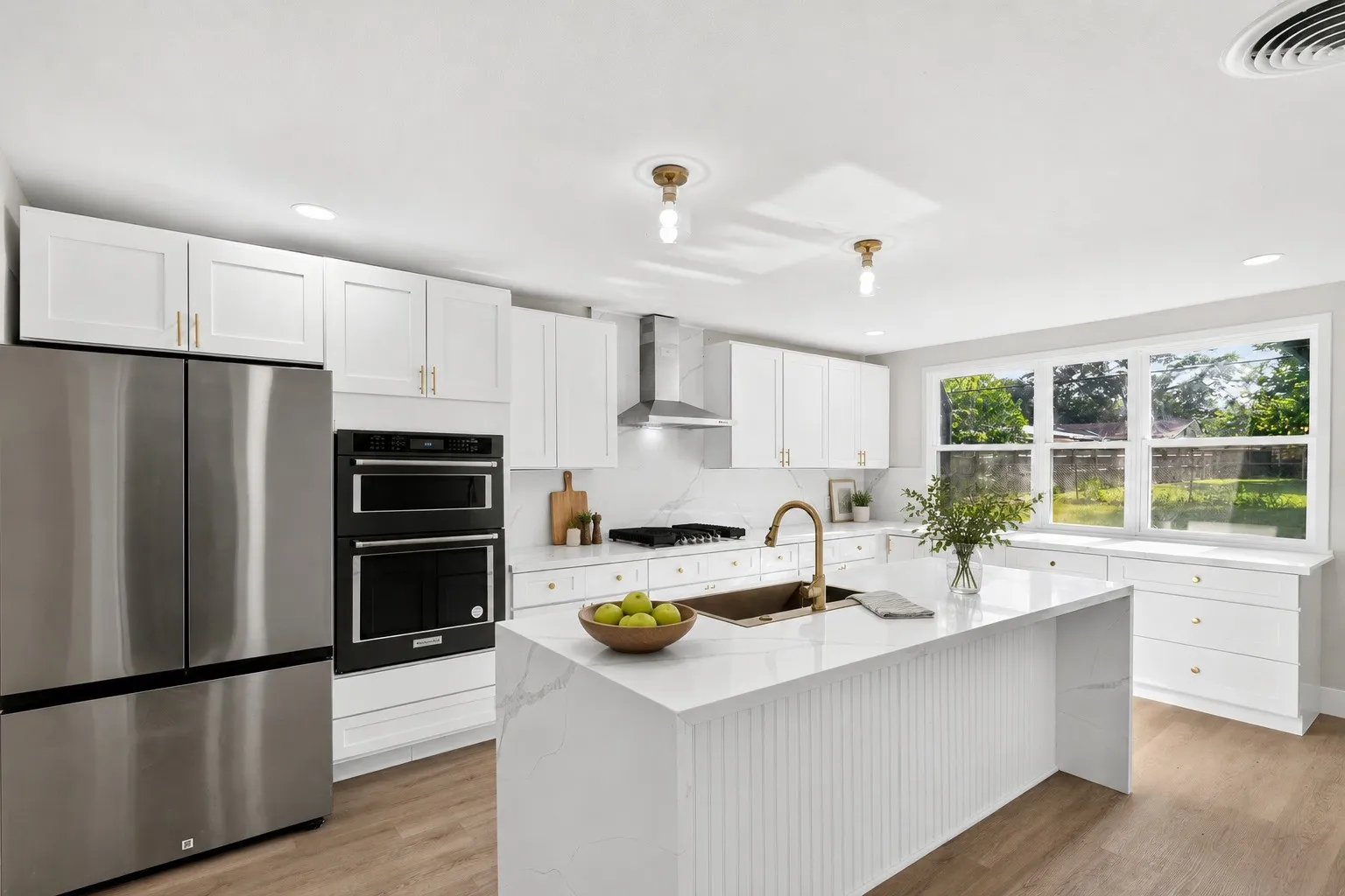 Kitchen featuring white shaker cabinetry, stainless steel appliances, a center island with a built-in sink, and wood-finish flooring