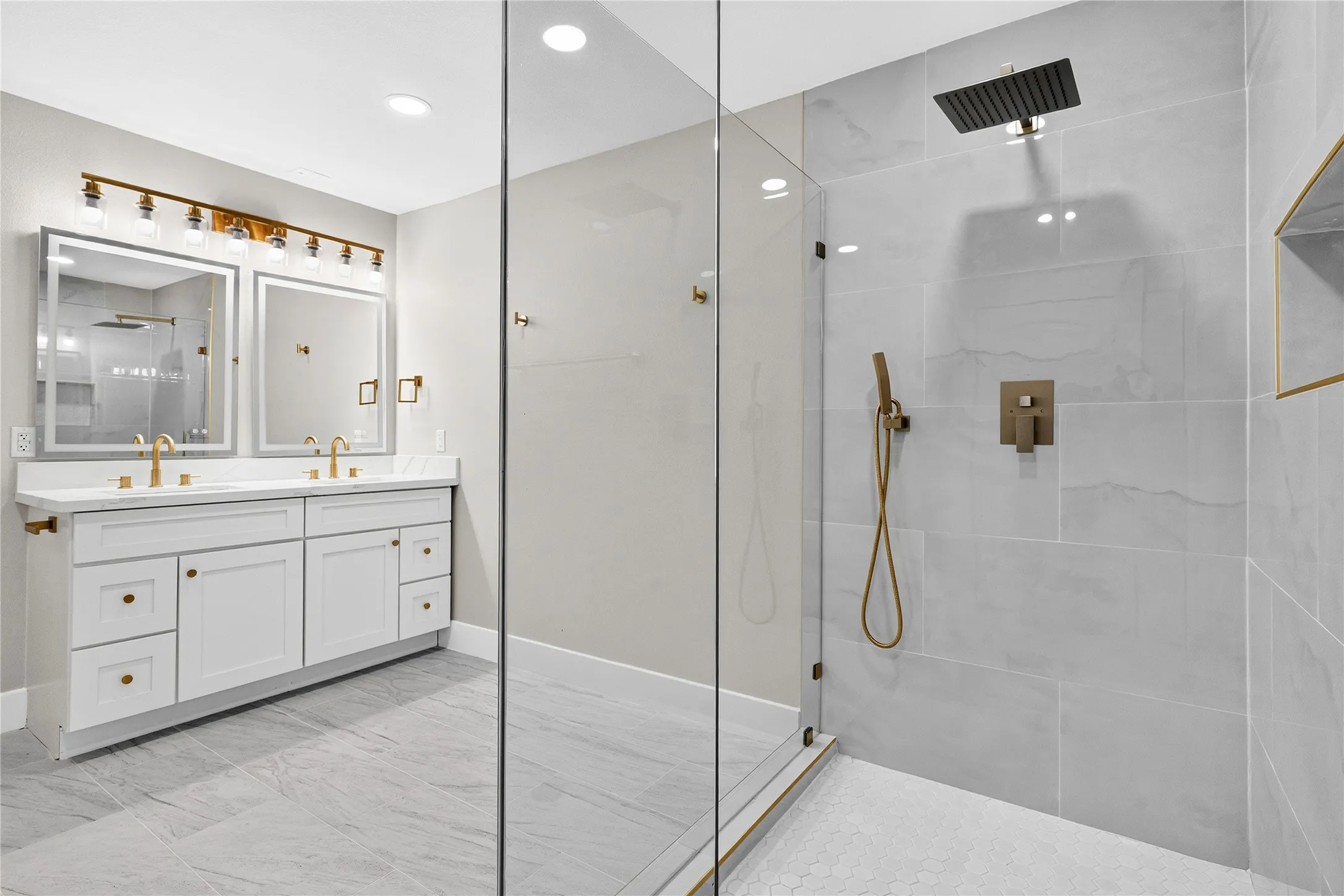 Dual vanity with undermount sinks, frameless glass shower enclosure, rainfall showerhead, handheld shower, and recessed shower niche