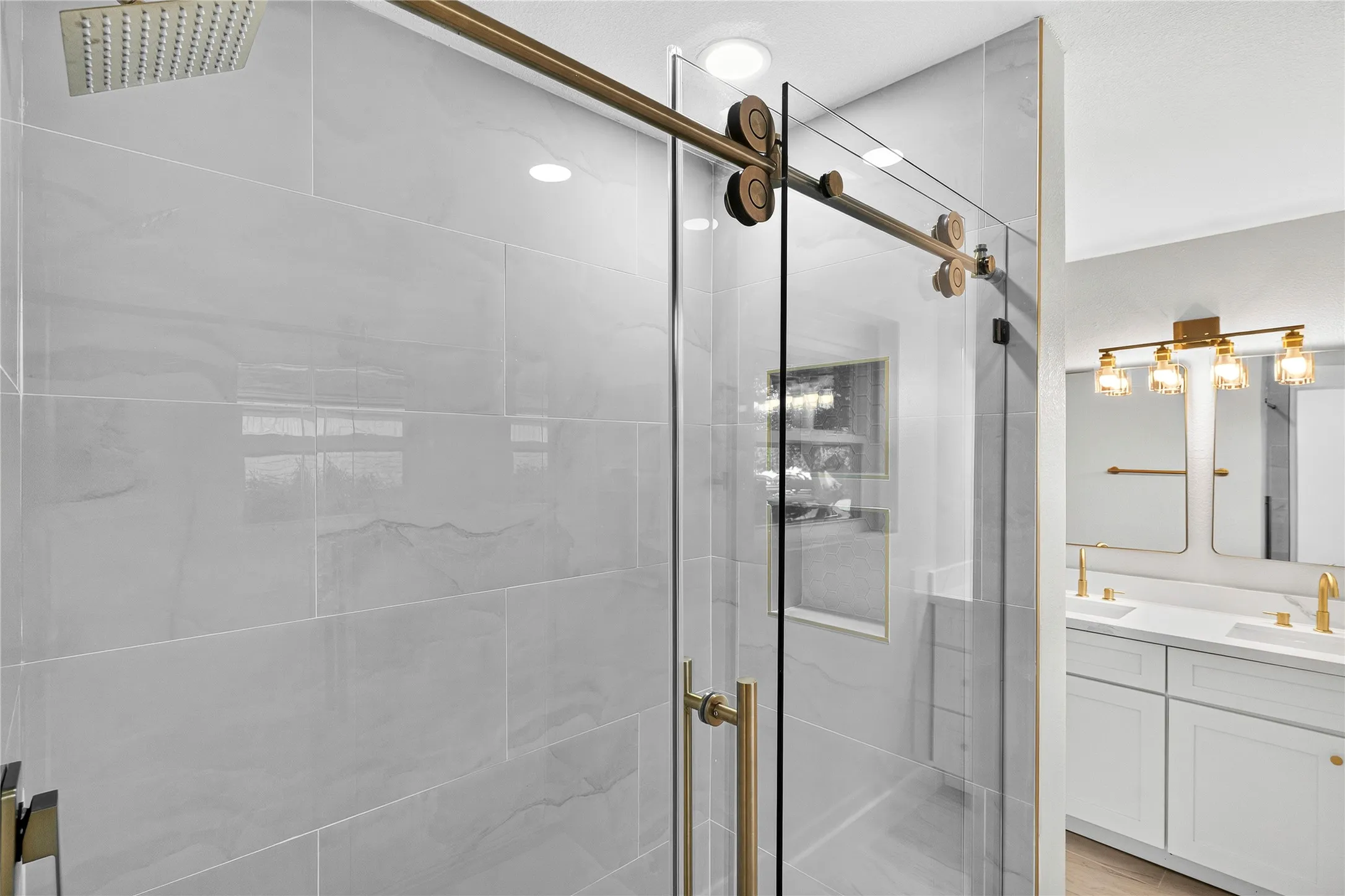 Rainfall showerhead, floor-to-ceiling large format tile, glass barn door shower enclosure, dual vanity with undermount sinks, and gold-finish fixtures