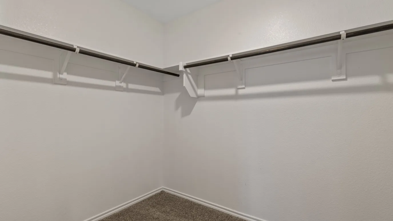 Built-in closet shelving and clothing rods with textured walls and carpet flooring