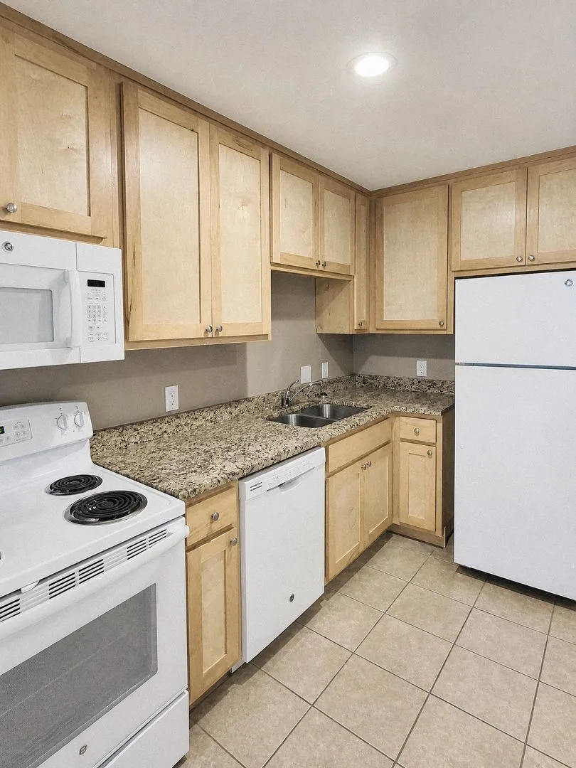 Kitchen featuring light wood-finish cabinetry, granite-style countertops, stainless steel double-basin sink, tile flooring, and recessed lighting