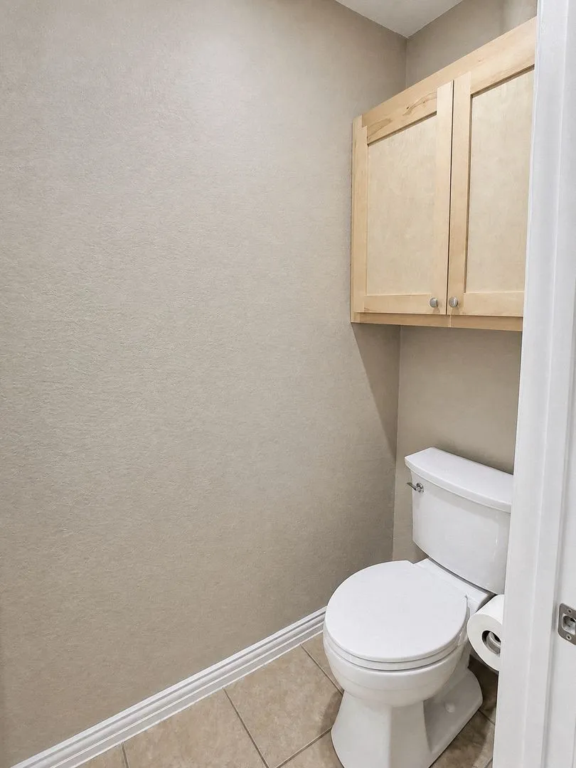 Built-in cabinetry with light-toned wood doors, ceramic tile flooring, and a white commode