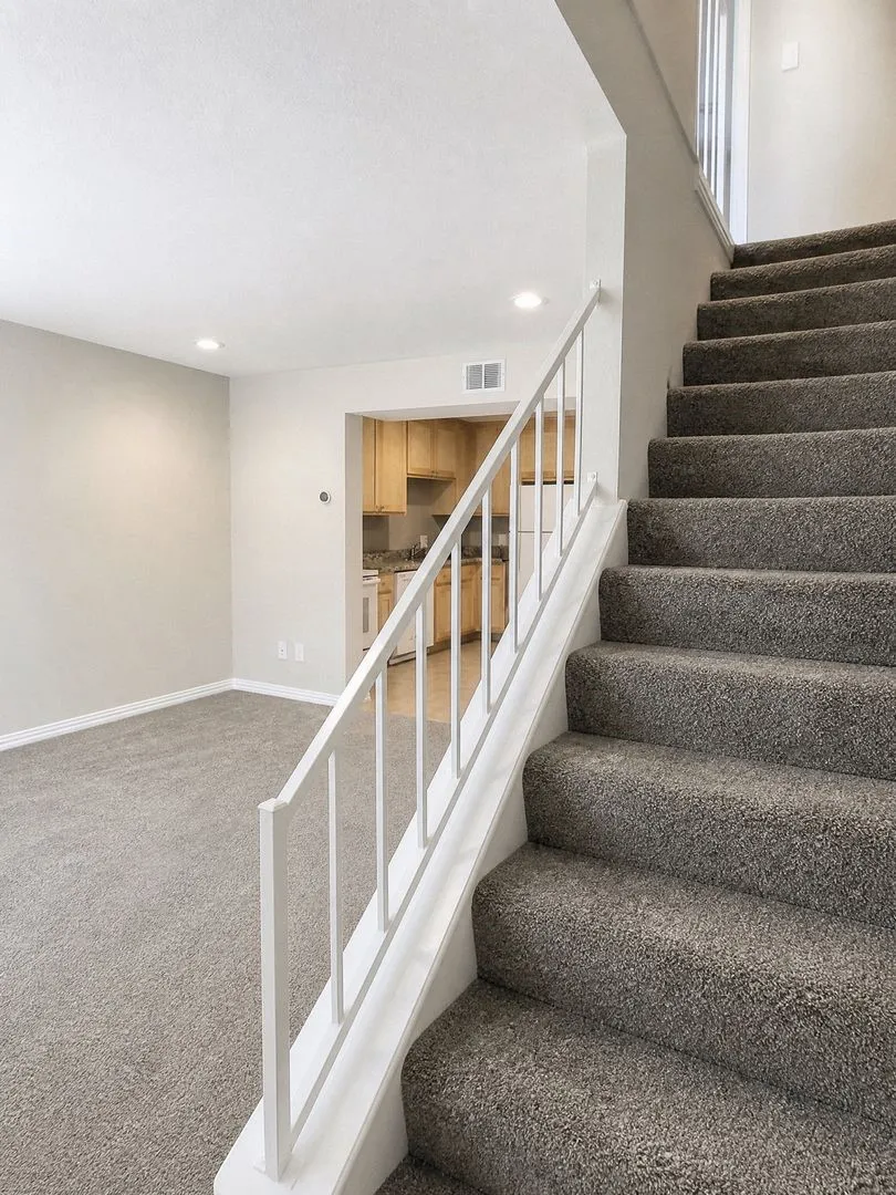 Carpeted staircase with white balusters, recessed lighting, and a neutral wall color