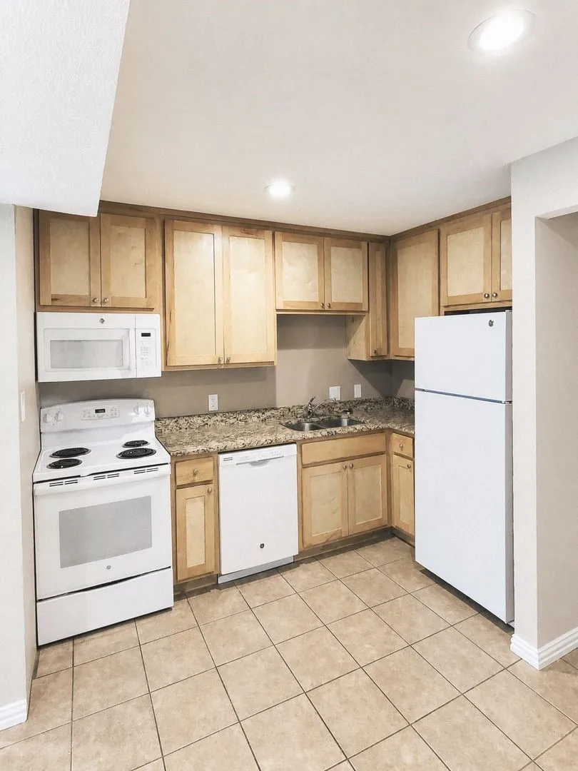 Kitchen featuring wood-finish cabinetry, light-toned countertop, white appliances, recessed lighting, and square tile flooring