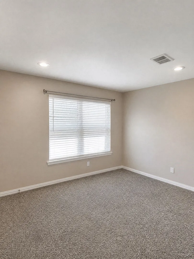 Recessed lighting, neutral-toned walls, window with blinds, and textured carpeting
