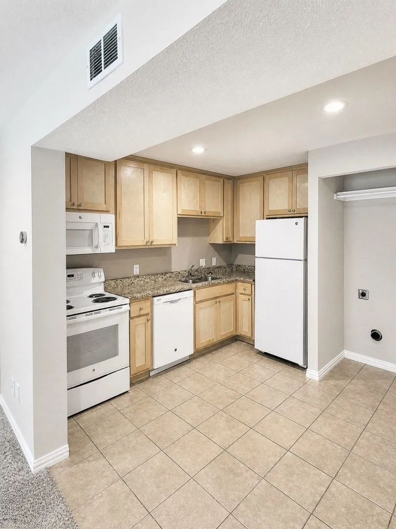 Kitchen featuring wood-finish cabinetry, granite-style countertops, and a full suite of white appliances including a refrigerator, range, microwave, and dishwasher