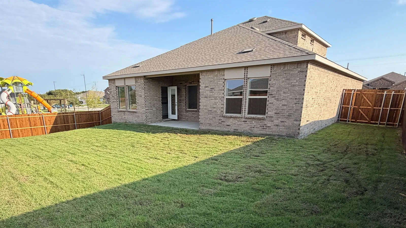 Expansive green lawn, privacy fencing, brick exterior, covered patio, and multi-pane windows