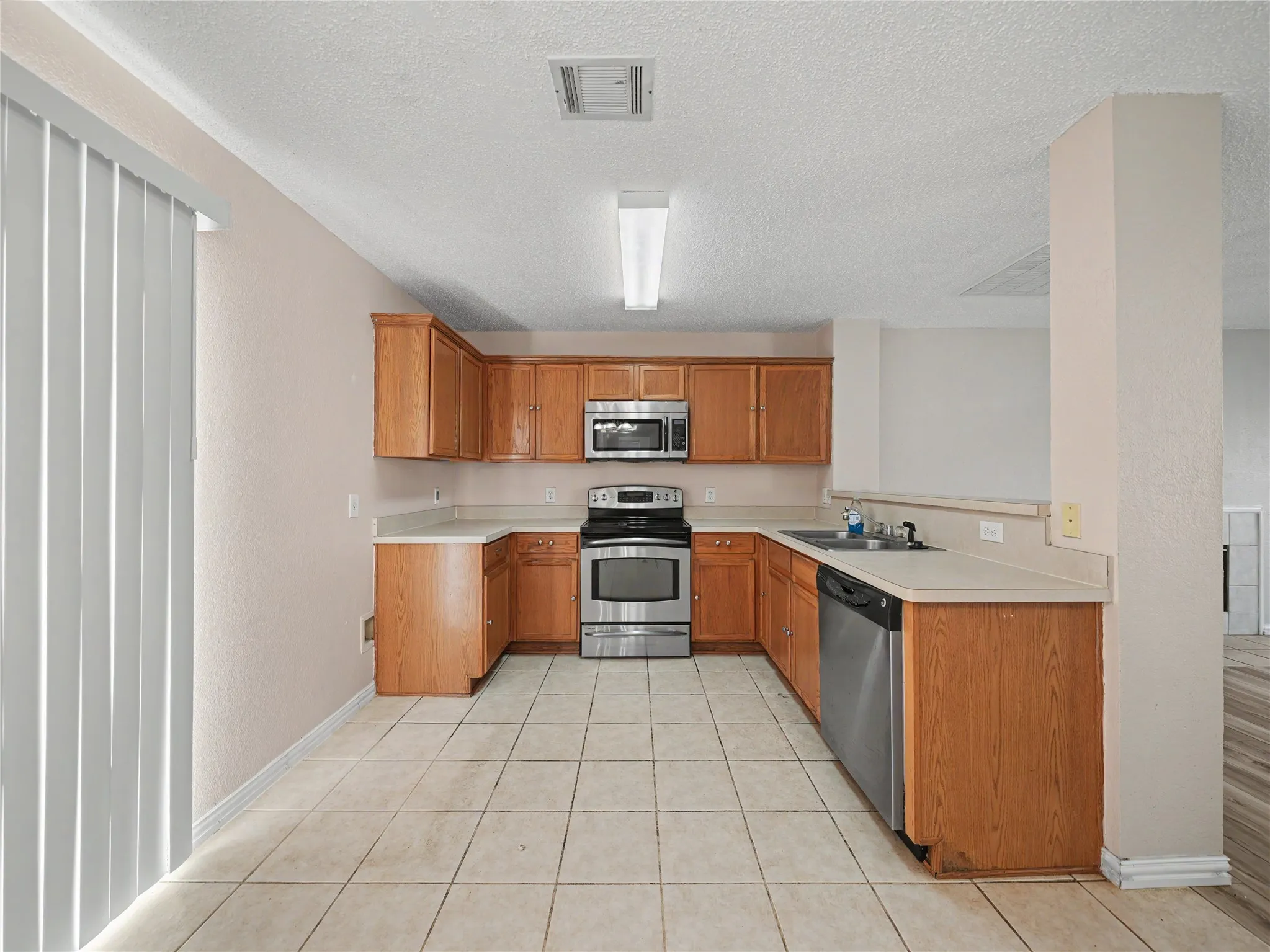 Kitchen featuring wood cabinetry, stainless steel appliances, light-toned countertops, and tiled flooring