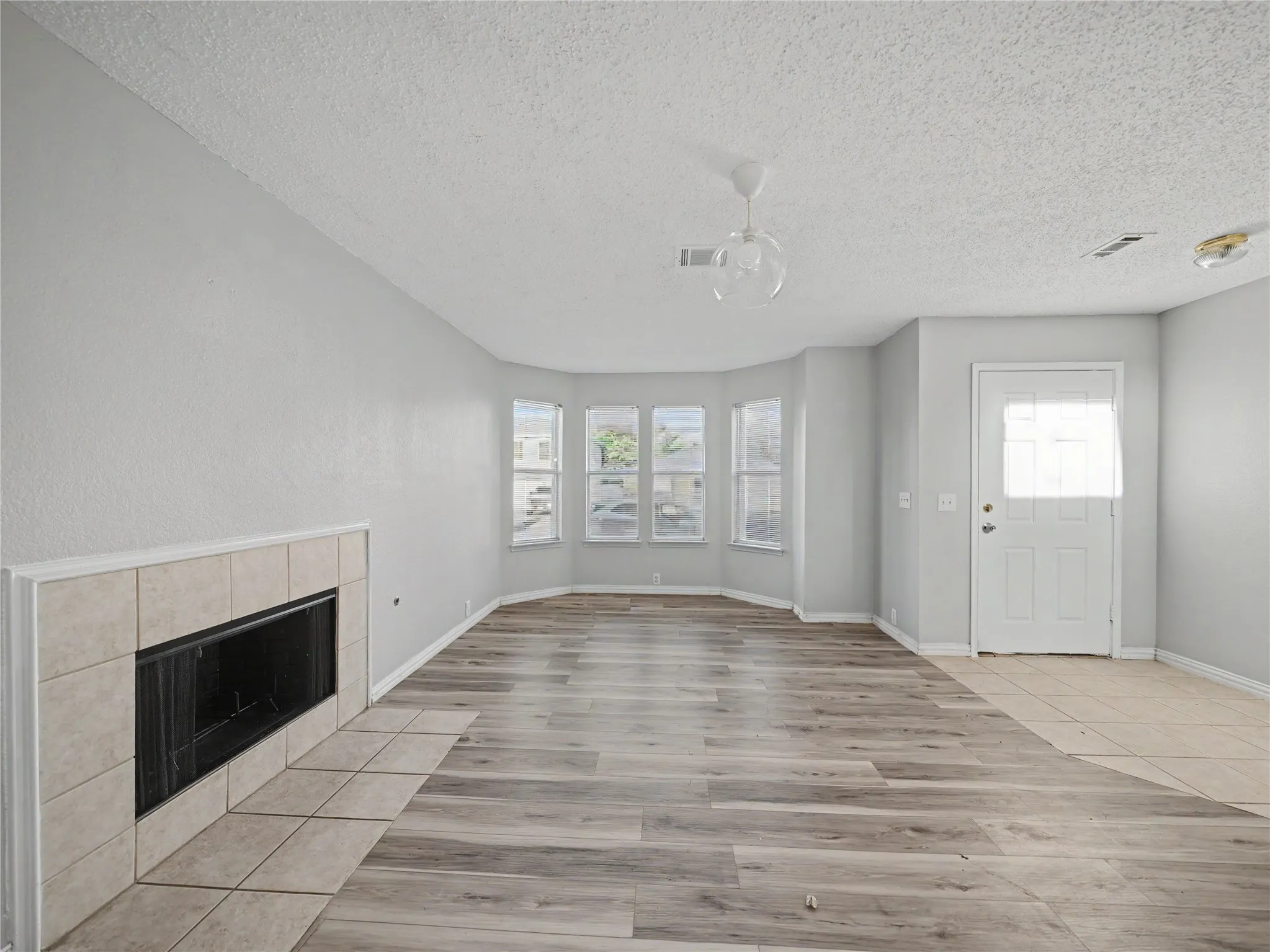 Living area with wood-finish flooring, a tiled fireplace, and a bay window