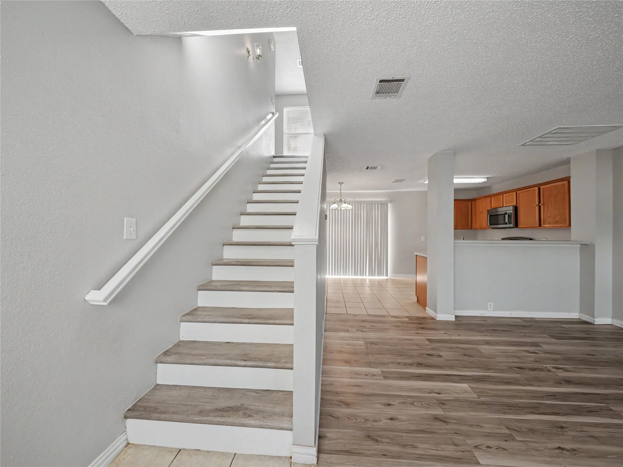 Wood-finish flooring, staircase with wood-finish treads, white handrail, tile flooring, and wood cabinetry