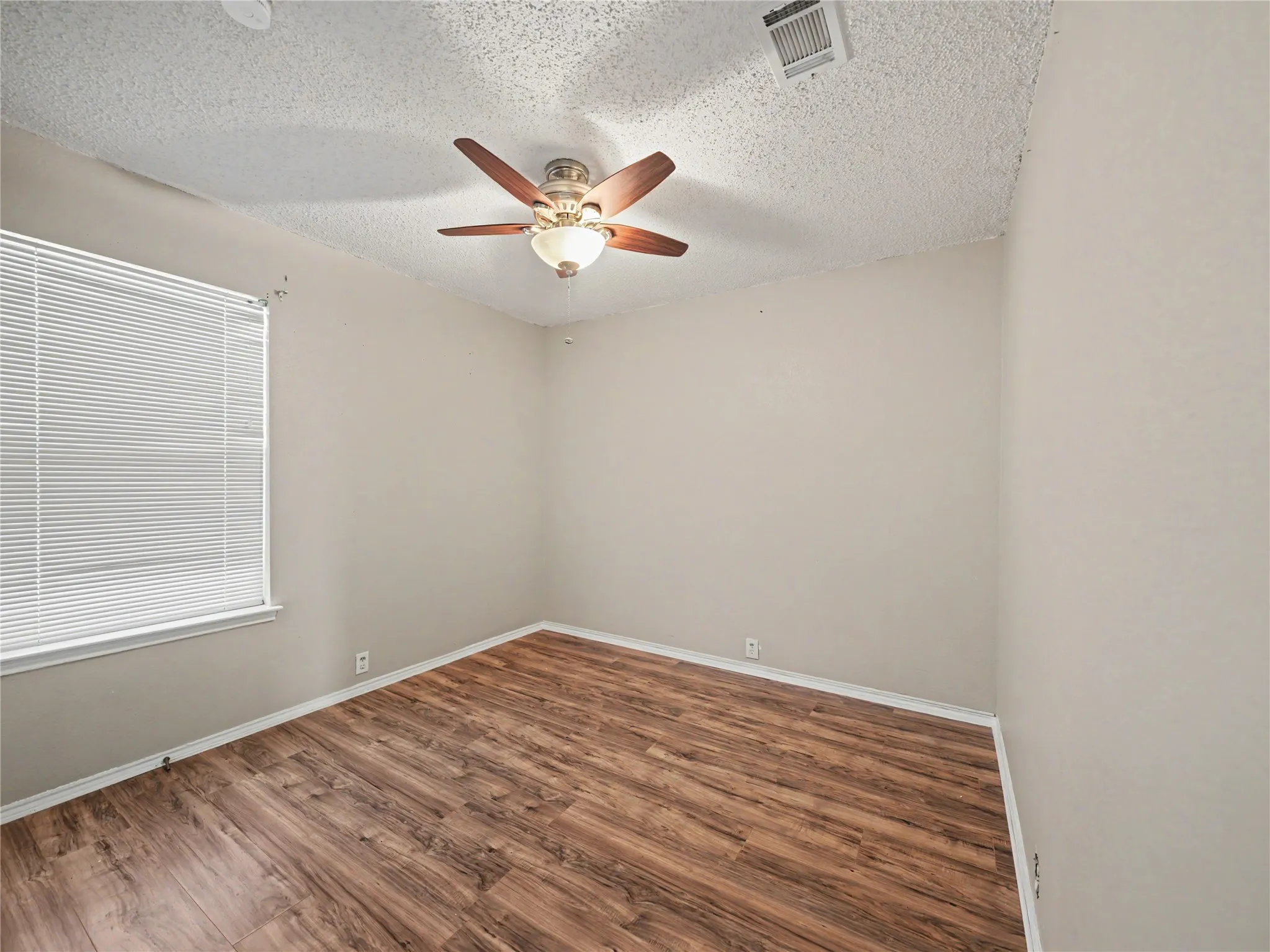 Wood-finish flooring, neutral wall paint, window with blinds, ceiling fan with light fixture, and overhead ventilation