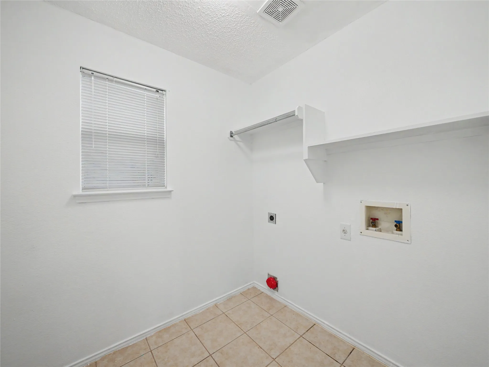 Laundry area featuring tile flooring, built-in shelving, a clothes hanging rod, and a window with blinds