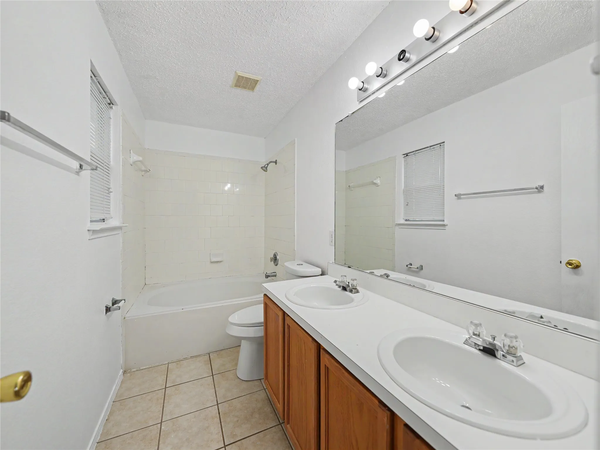 Bathroom featuring a dual sink vanity with wood-finish cabinetry, tile flooring, a built-in bathtub with tile surround, and an integrated wall mirror