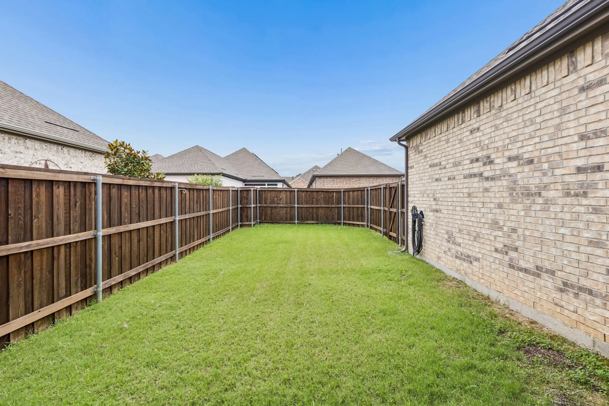 Expansive grassy backyard featuring a full perimeter privacy fence and a brick exterior