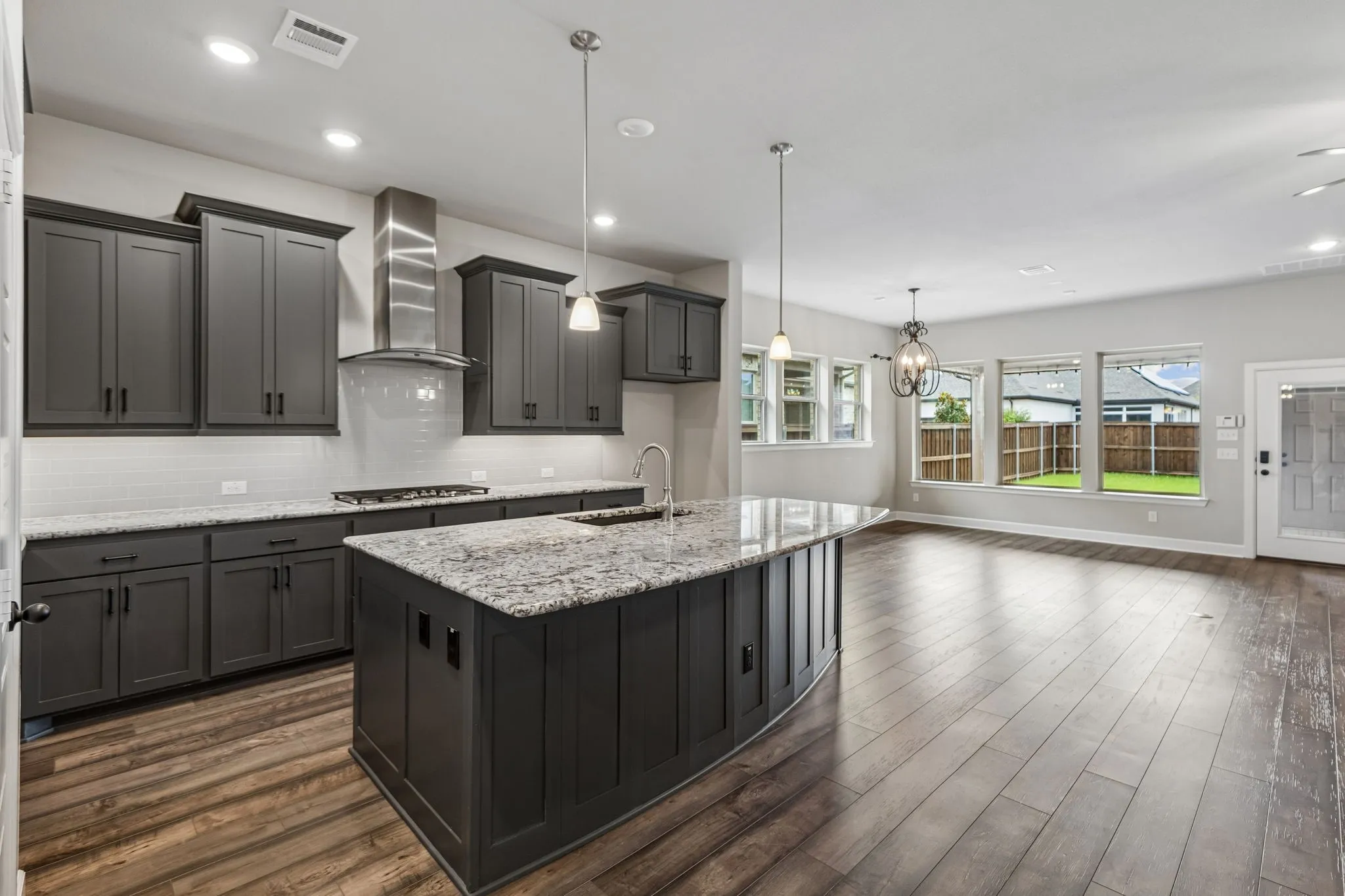 Open-concept kitchen with dark cabinetry, granite countertops, a central island, and wood-finish flooring