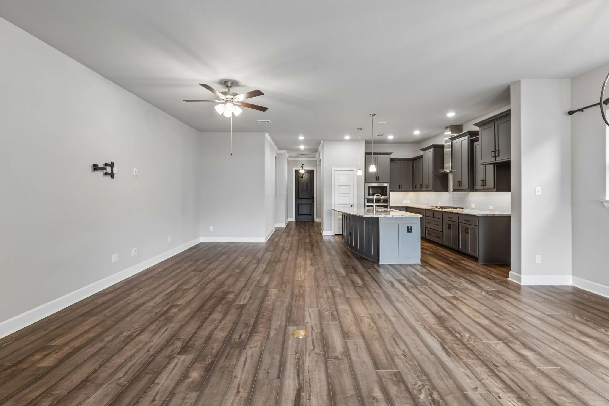 Open-concept living space featuring wood-finish flooring, a ceiling fan, a kitchen island with pendant lighting, dark wood cabinetry, and stainless steel appliances