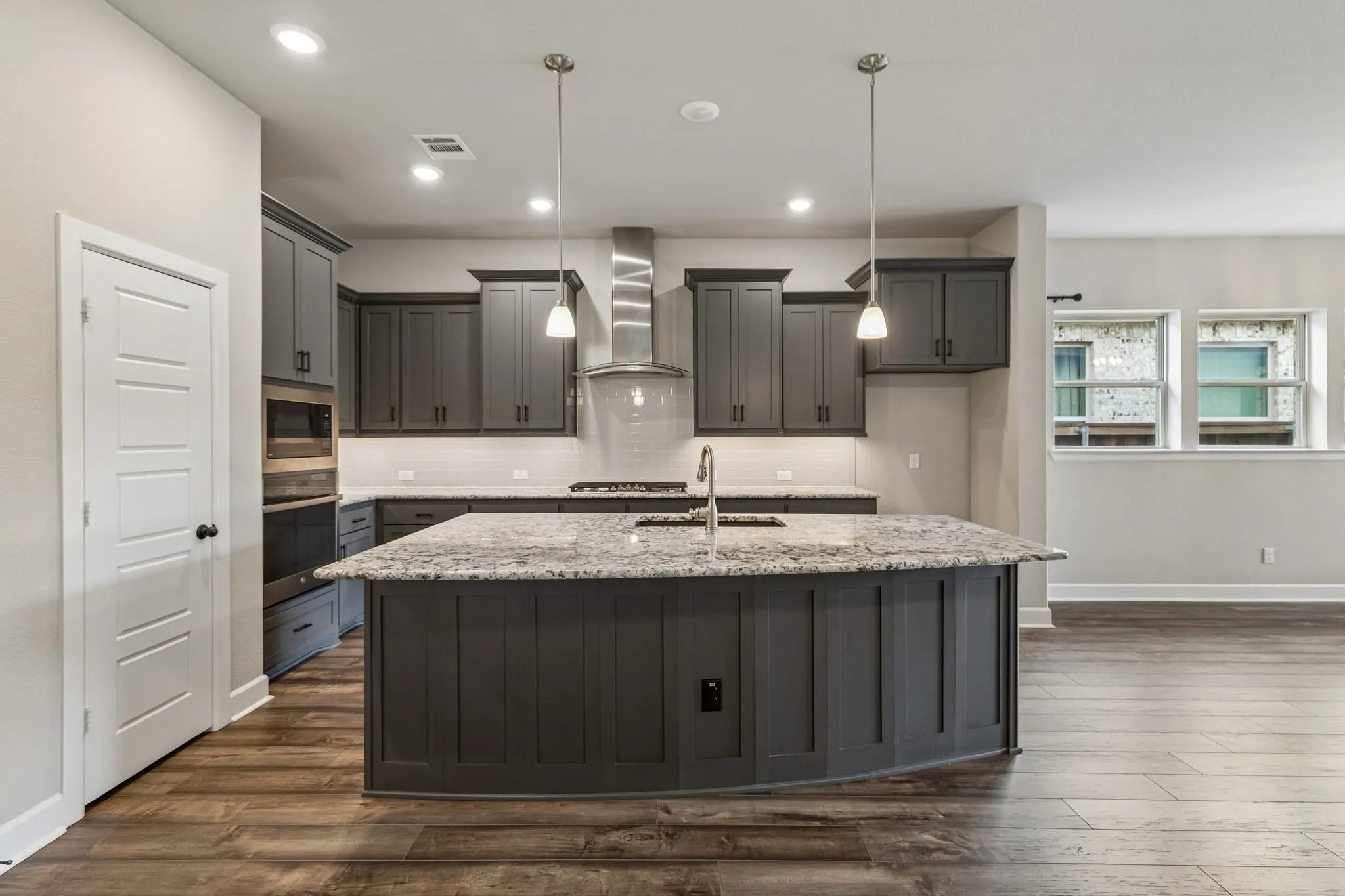 Kitchen featuring a large island with sink, stainless steel appliances, dark wood-finish flooring, recessed lighting, and pendant lighting