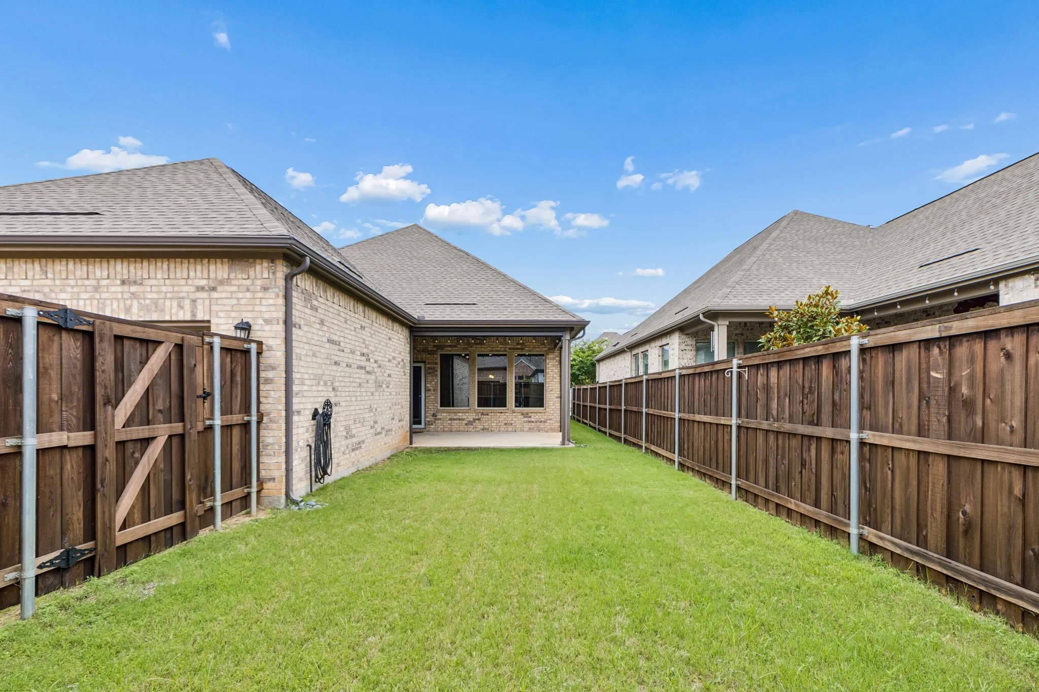 Expansive backyard featuring a manicured lawn, brick exterior, covered patio, and wood privacy fence