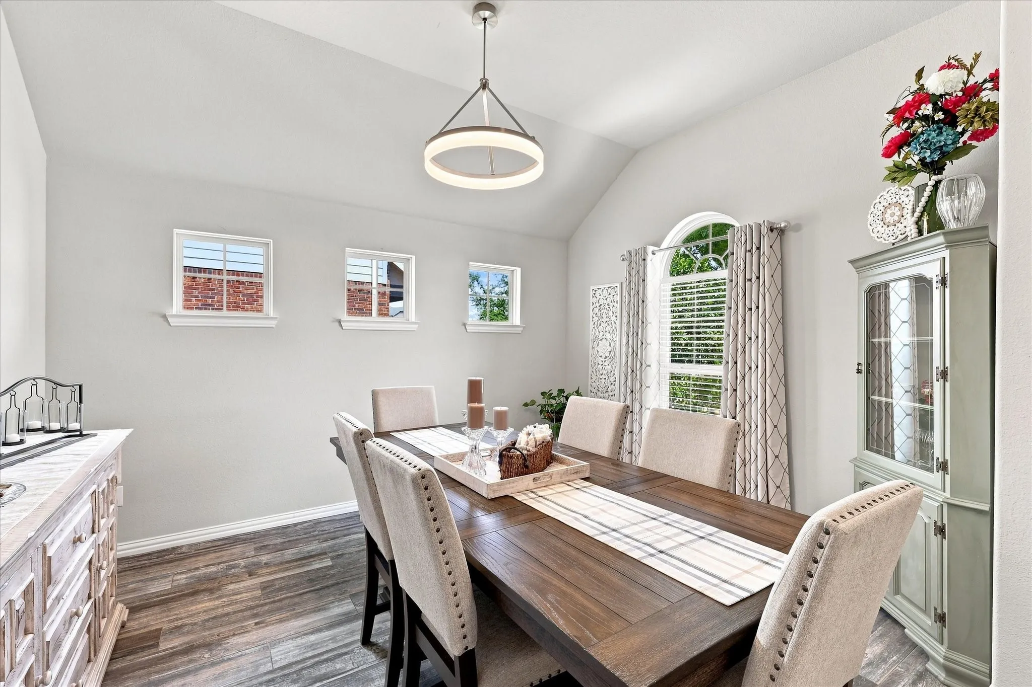 Formal Dining Room features a Vaulted Ceiling, Contemporary Designer Lighting, Upgraded Wood-look Tile Flooring and Abundant Natural Light. The Open Design and Architectural Details create an Impressive Space for Entertaining.