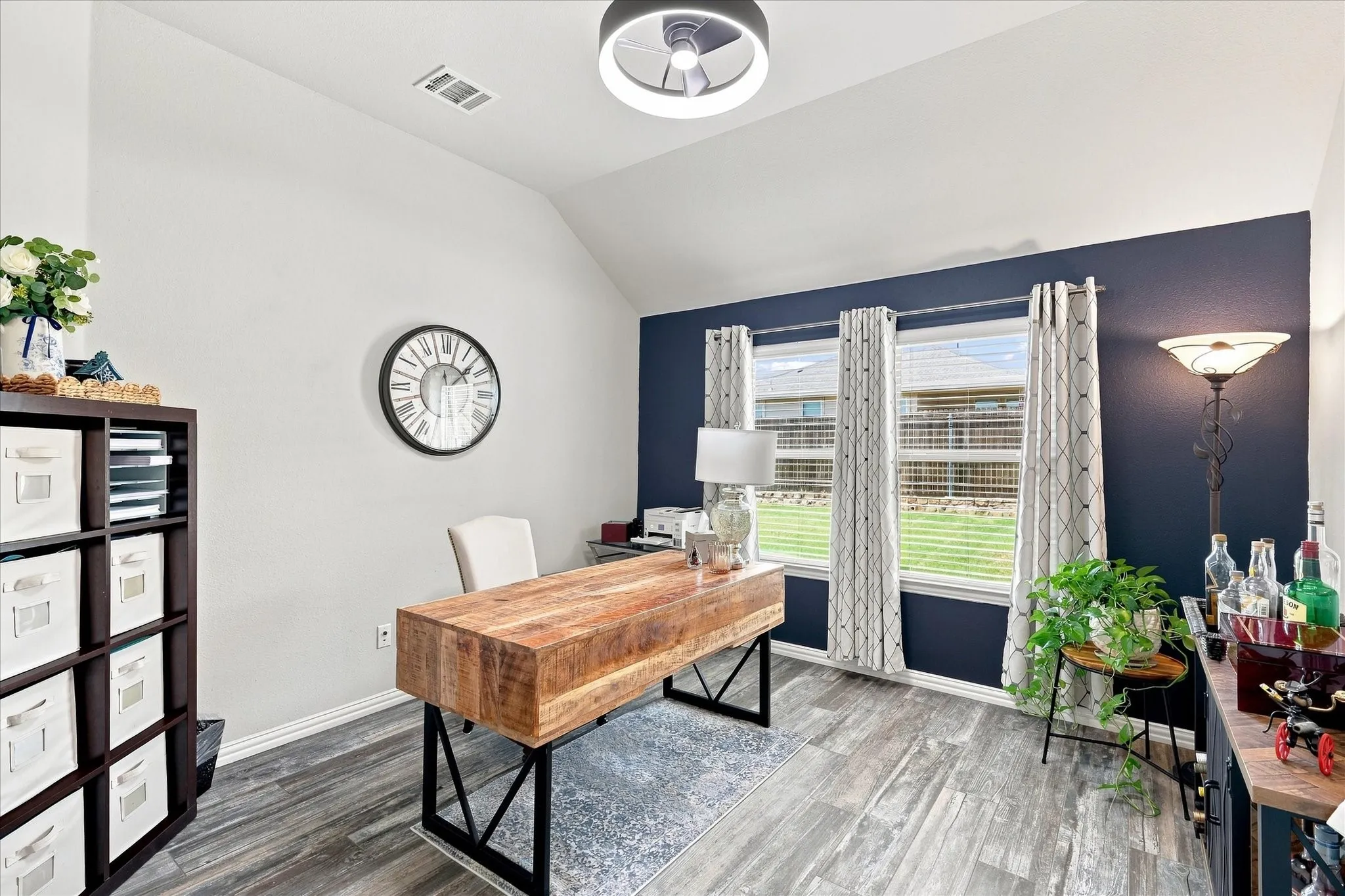 Spacious Den/Home Office features a Vaulted Ceiling, Modern Ceiling Fan, Abundant Natural Light, Upgraded Wood-Look Tile Flooring and a Dramatic Accent Wall.