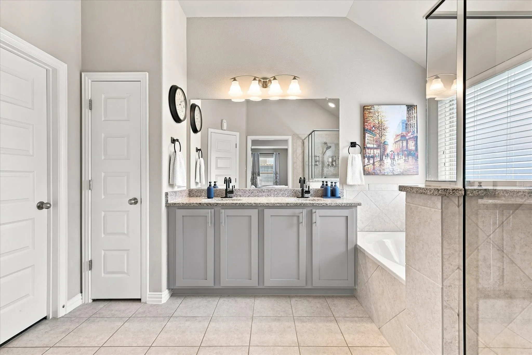 Spacious Primary Bath features a Vaulted Ceiling, Dual-sink Granite Mirrored Vanity, Abundant Cabinetry, Tile Flooring. A Deep Soaking Tub with Tiled Surround Complemented by a Separate Tiled Walk-in Shower with Frameless Glass Enclosure and Built-in Corner Shelves. There's also Convenient Access to the Linen and Walk-in Closets.