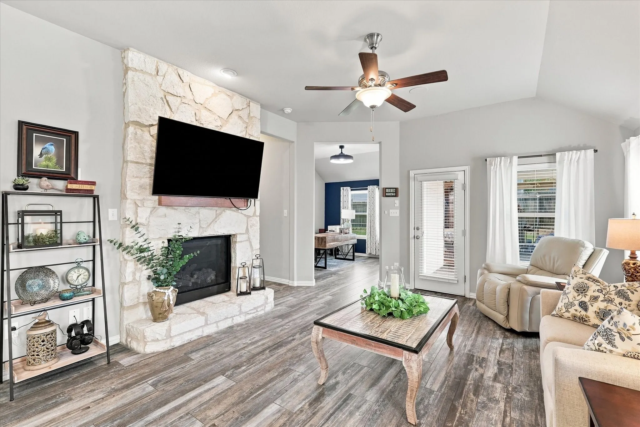 Spacious Living Room with Vaulted Ceiling, Floor-to-Ceiling Natural Stone Gas Fireplace, Wood-look Tile Floors and Abundant Windows. The Open Design flows into the Casual Dining and Kitchen with Easy Access to Large Covered Outdoor Living and Private Fenced Back Yard.