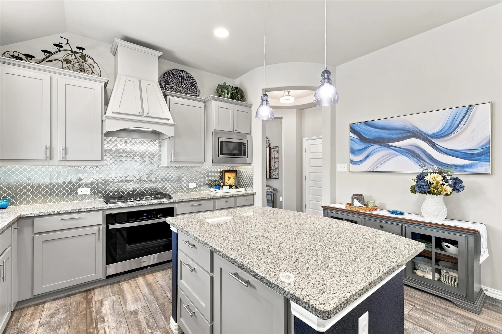 Cook’s Kitchen features Soaring Ceilings, Abundant Cabinetry, Granite Countertops, Decorative Tile Backsplash, Stainless Appliances, Gas Cooktop, Built-in Microwave and Oven, Recessed lLghting, and Wood-look Tile Flooring. A Large Center Island Provides Generous Prep and Serving Space, Breakfast Bar Seating, and Stylish Pendant Lighting.