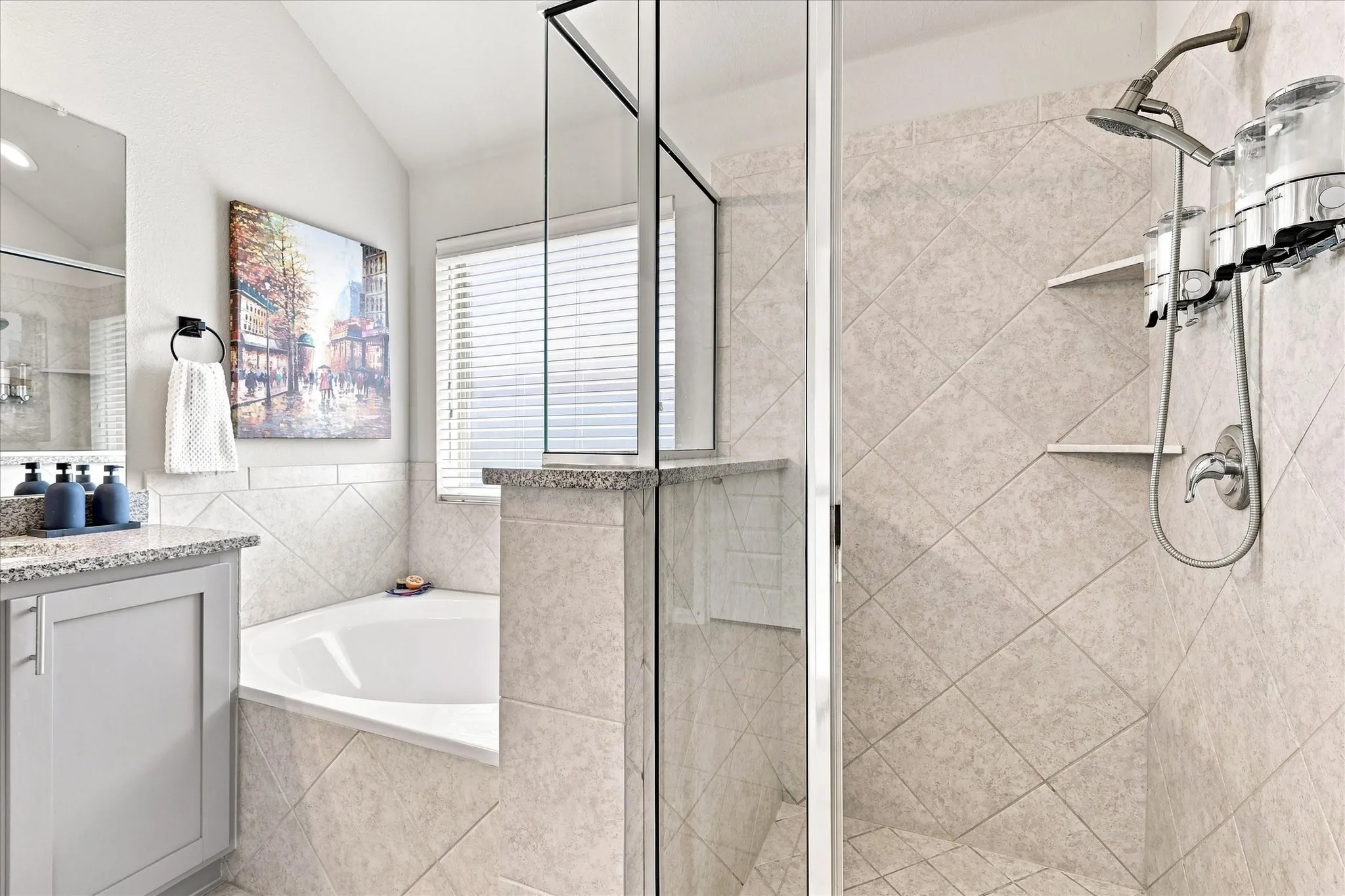 Spacious Primary Bath features a Vaulted Ceiling, Dual-sink Granite Mirrored Vanity, Abundant Cabinetry, Tile Flooring. A Deep Soaking Tub with Tiled Surround Complemented by a Separate Tiled Walk-in Shower with Frameless Glass Enclosure and Built-in Corner Shelves. There's also Convenient Access to the Linen and Walk-in Closets.