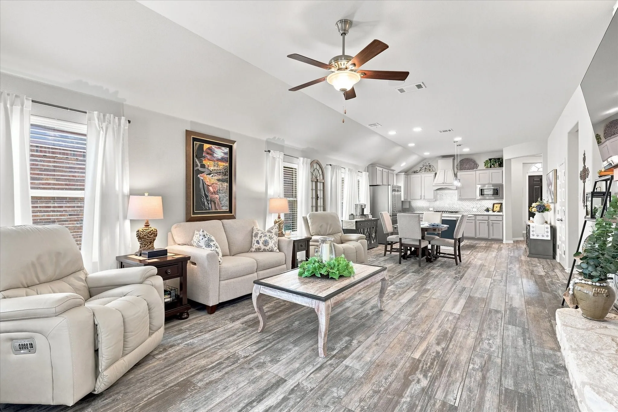 Spacious Living Room with Vaulted Ceiling, Floor-to-Ceiling Natural Stone Gas Fireplace, Wood-look Tile Floors and Abundant Windows. The Open Design flows into the Casual Dining and Kitchen with Easy Access to Large Covered Outdoor Living and Private Fenced Back Yard.