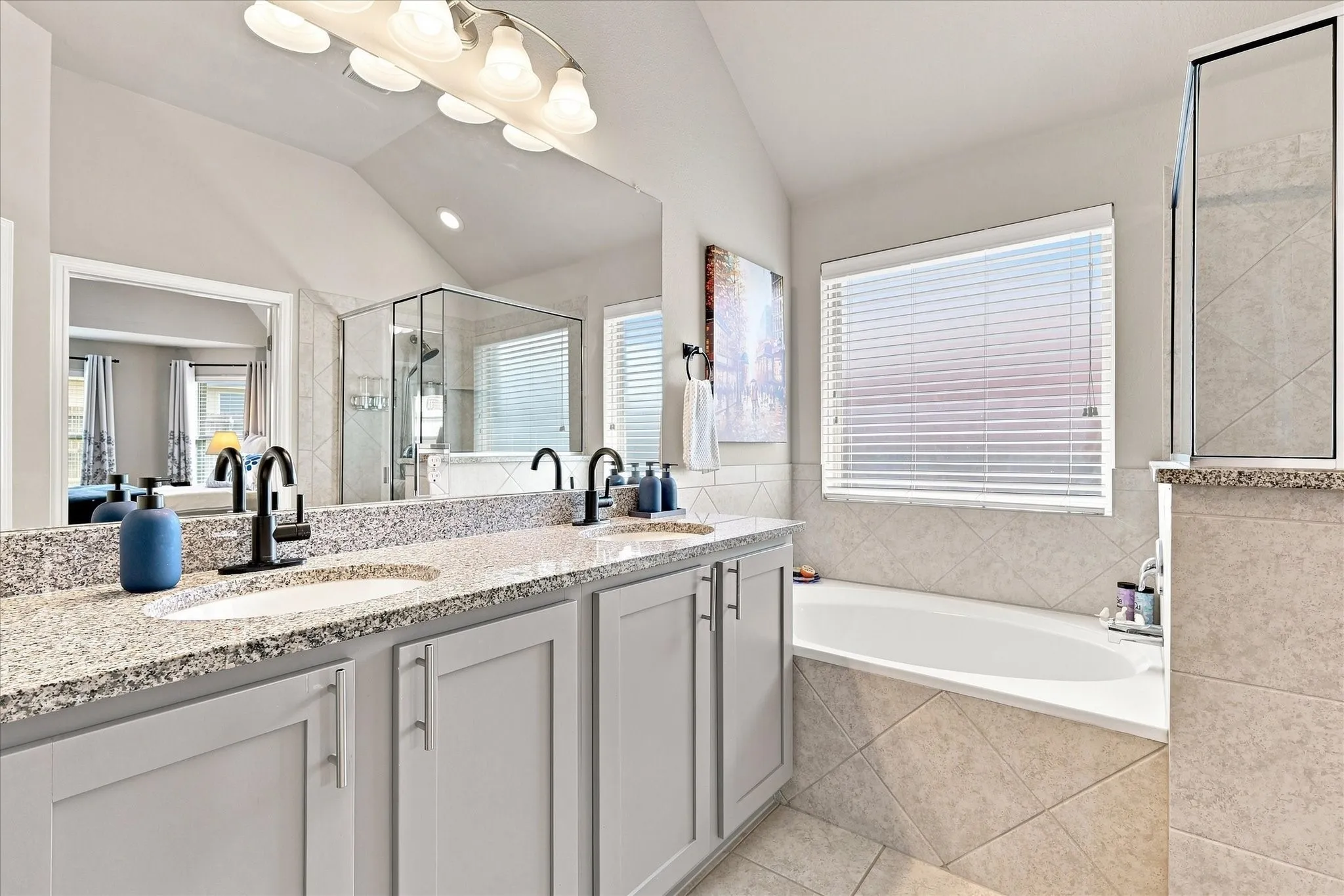 Spacious Primary Bath features a Vaulted Ceiling, Dual-sink Granite Mirrored Vanity, Abundant Cabinetry, Tile Flooring. A Deep Soaking Tub with Tiled Surround Complemented by a Separate Tiled Walk-in Shower with Frameless Glass Enclosure and Built-in Corner Shelves. There's also Convenient Access to the Linen and Walk-in Closets.