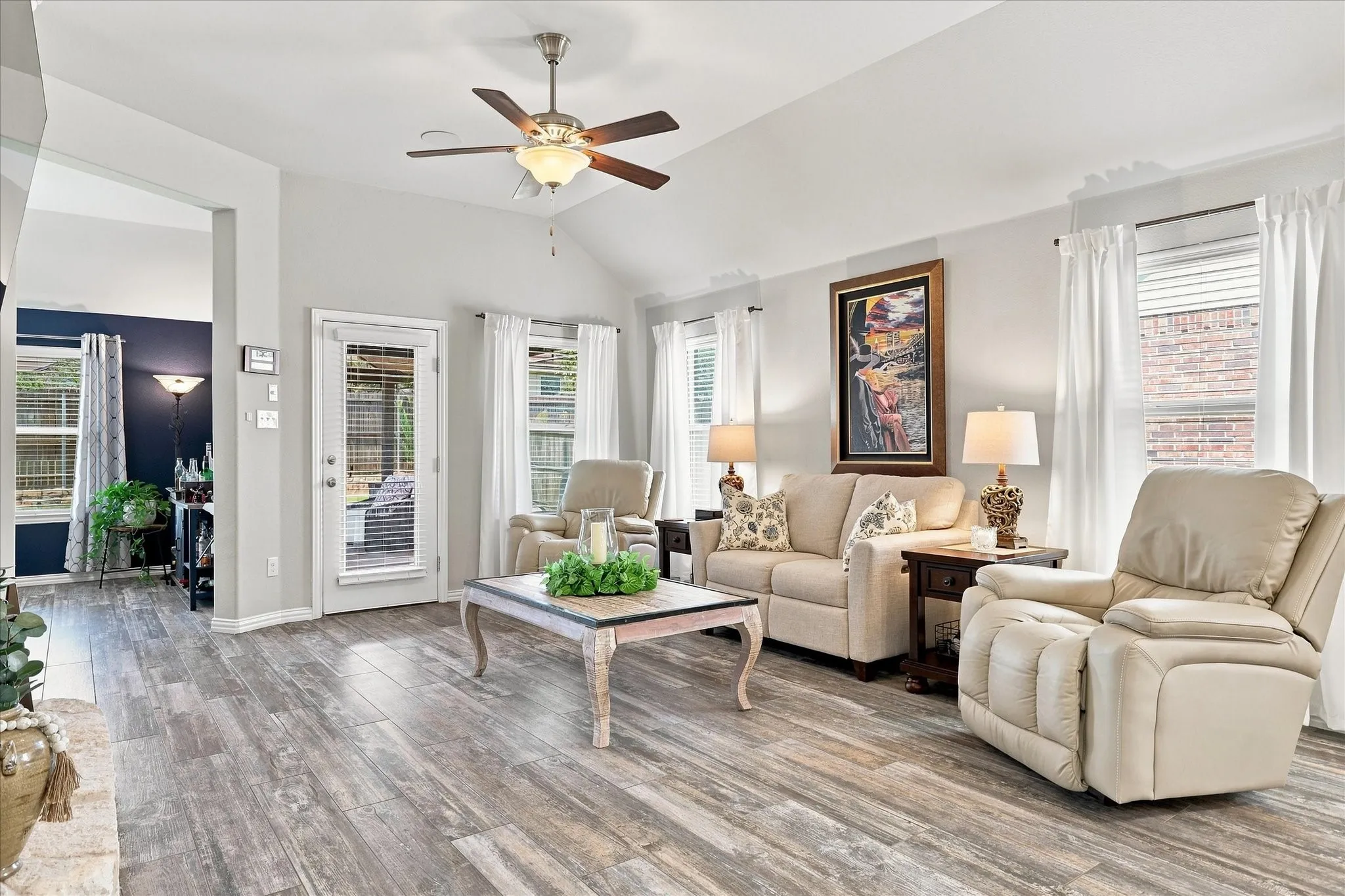 Spacious Living Room with Vaulted Ceiling, Floor-to-Ceiling Natural Stone Gas Fireplace, Wood-look Tile Floors and Abundant Windows. The Open Design flows into the Casual Dining and Kitchen with Easy Access to Large Covered Outdoor Living and Private Fenced Back Yard.