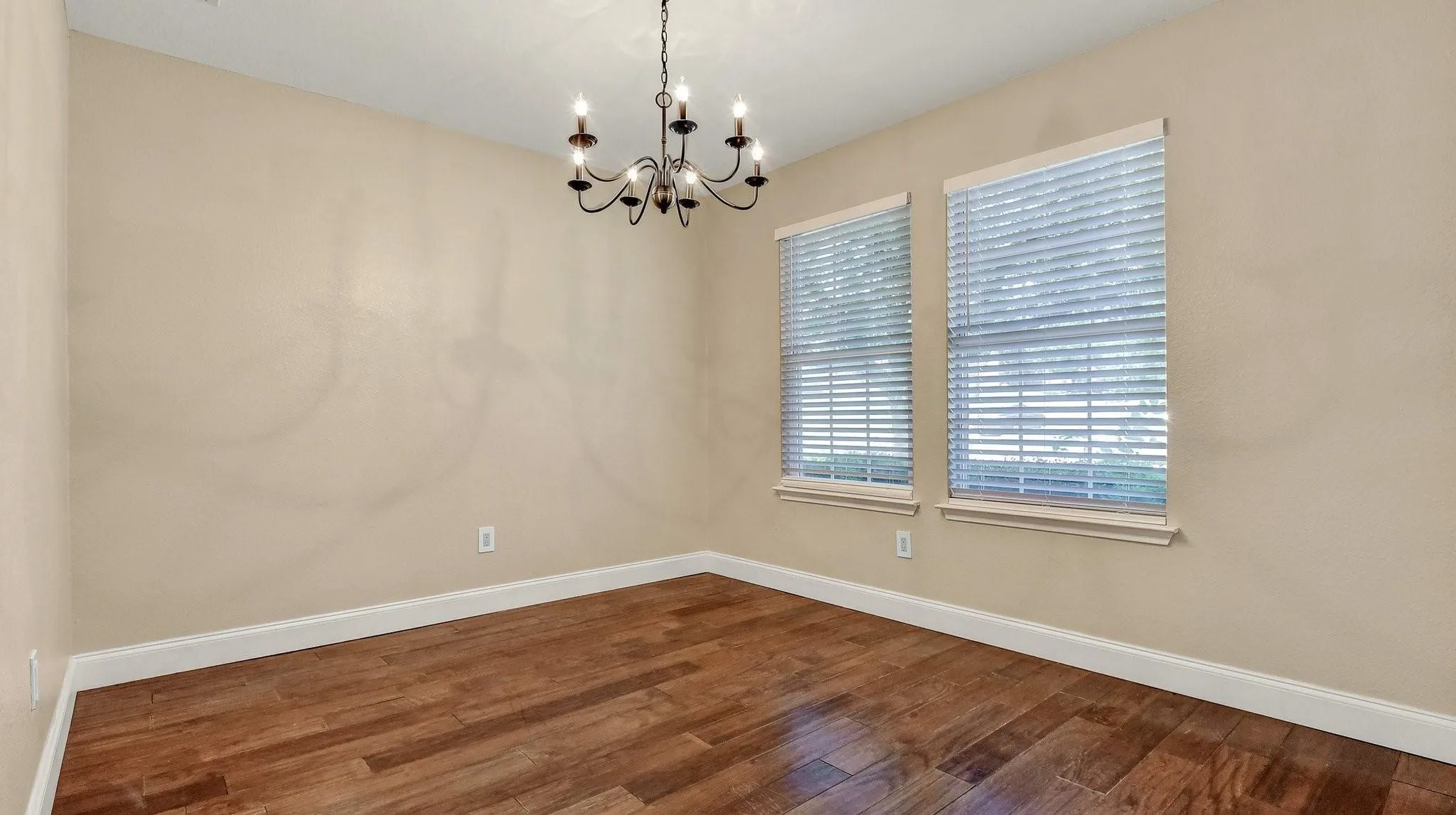 Wood-finish flooring, two windows with blinds, a dark-toned chandelier, and light-toned wall paint