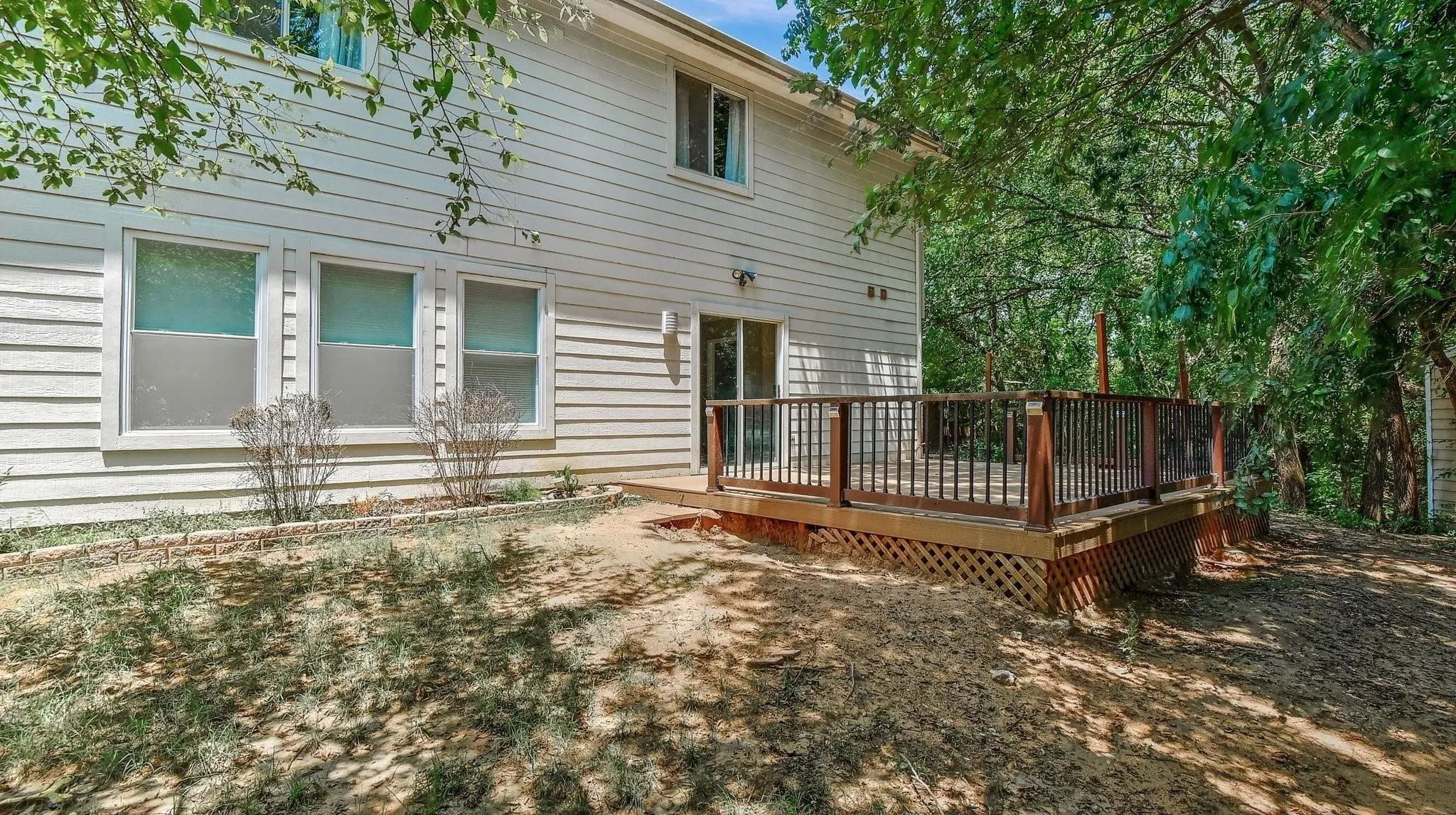 Exterior siding, multiple windows, sliding glass door, and a wooden deck with lattice skirting