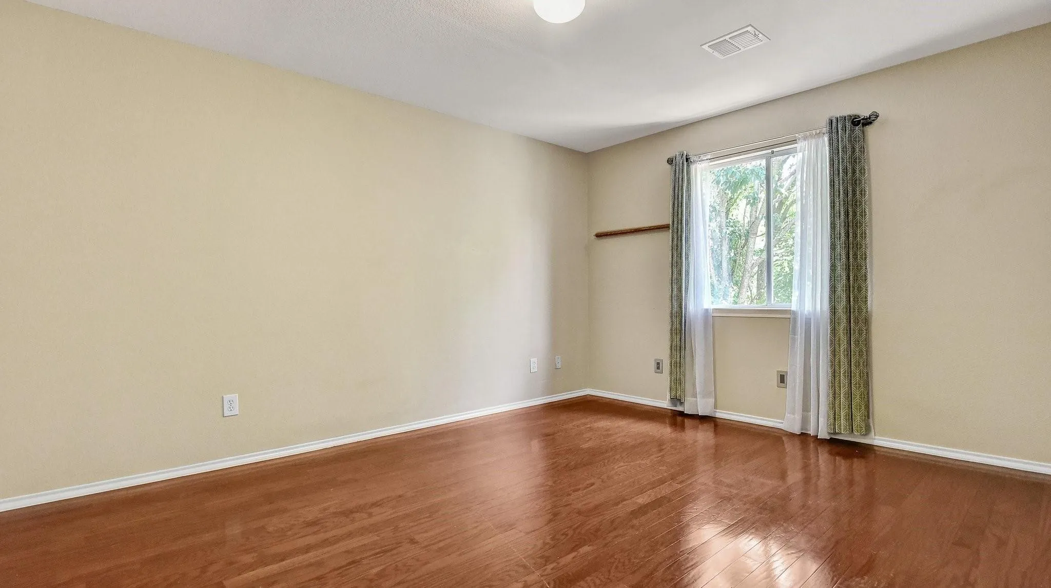 Wood-finish flooring, neutral wall tones, and a window with a wood curtain rod