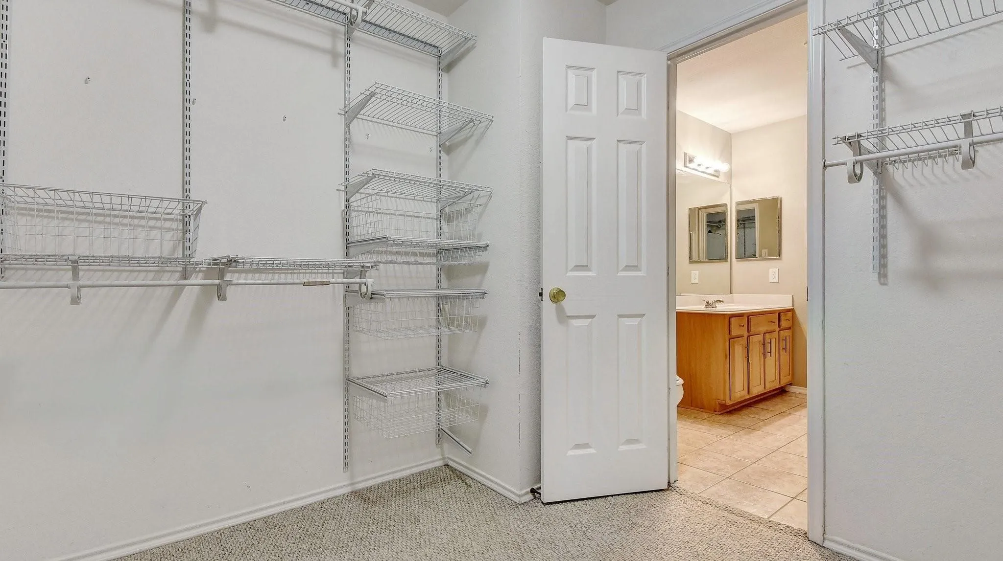 Customizable wire shelving system, carpeted flooring, wood-finish vanity, light-toned countertop, and tiled flooring